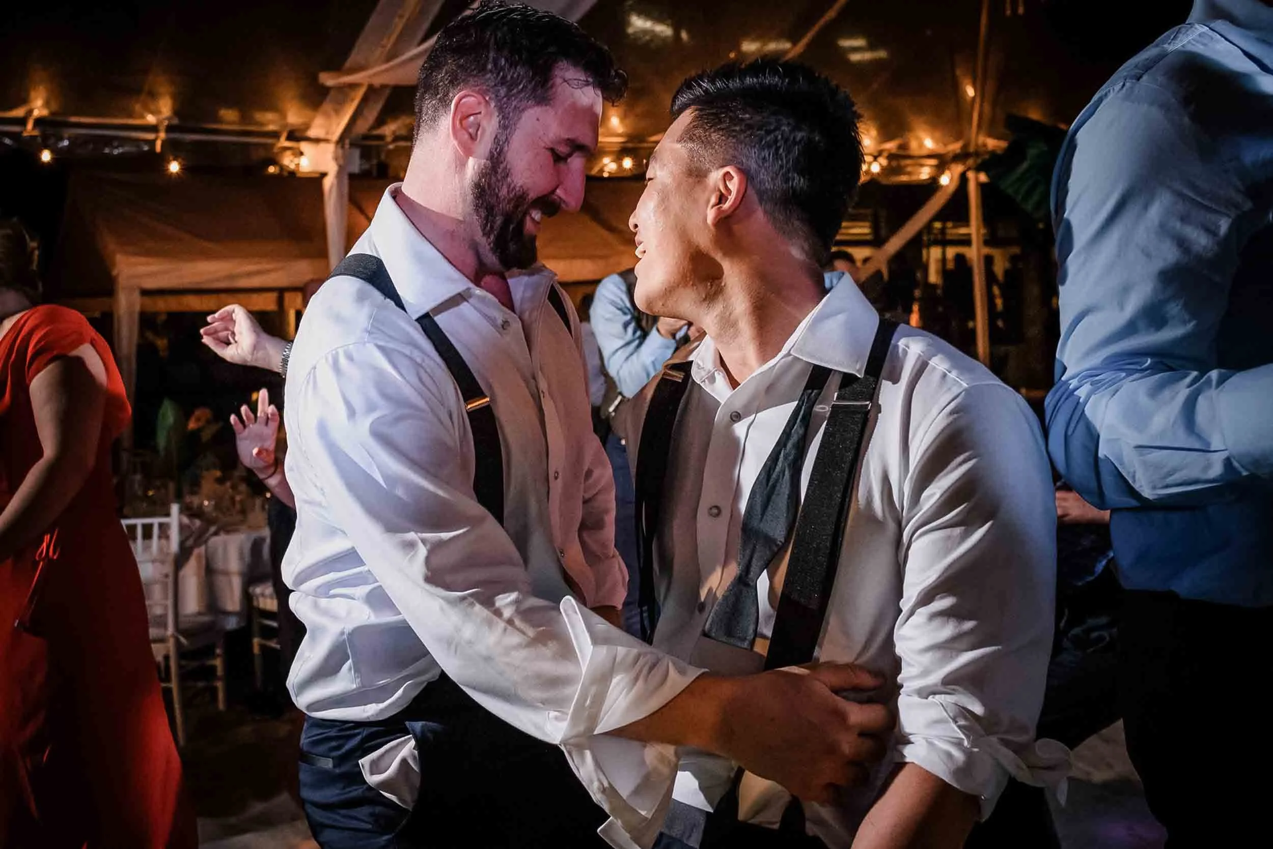 Groom are dancing closely at their wedding reception, smiling and looking at each other. 