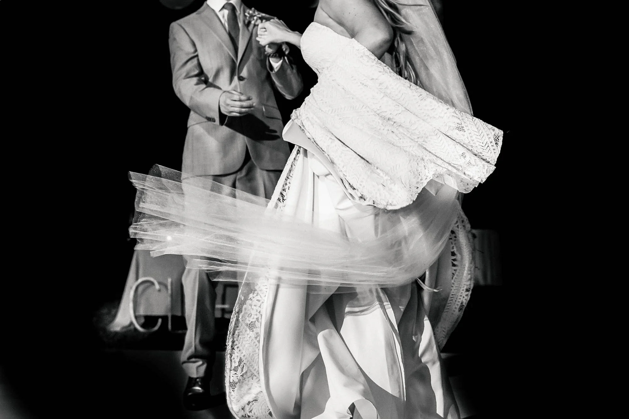 Bride and groom dancing at beach wedding with veil movement.