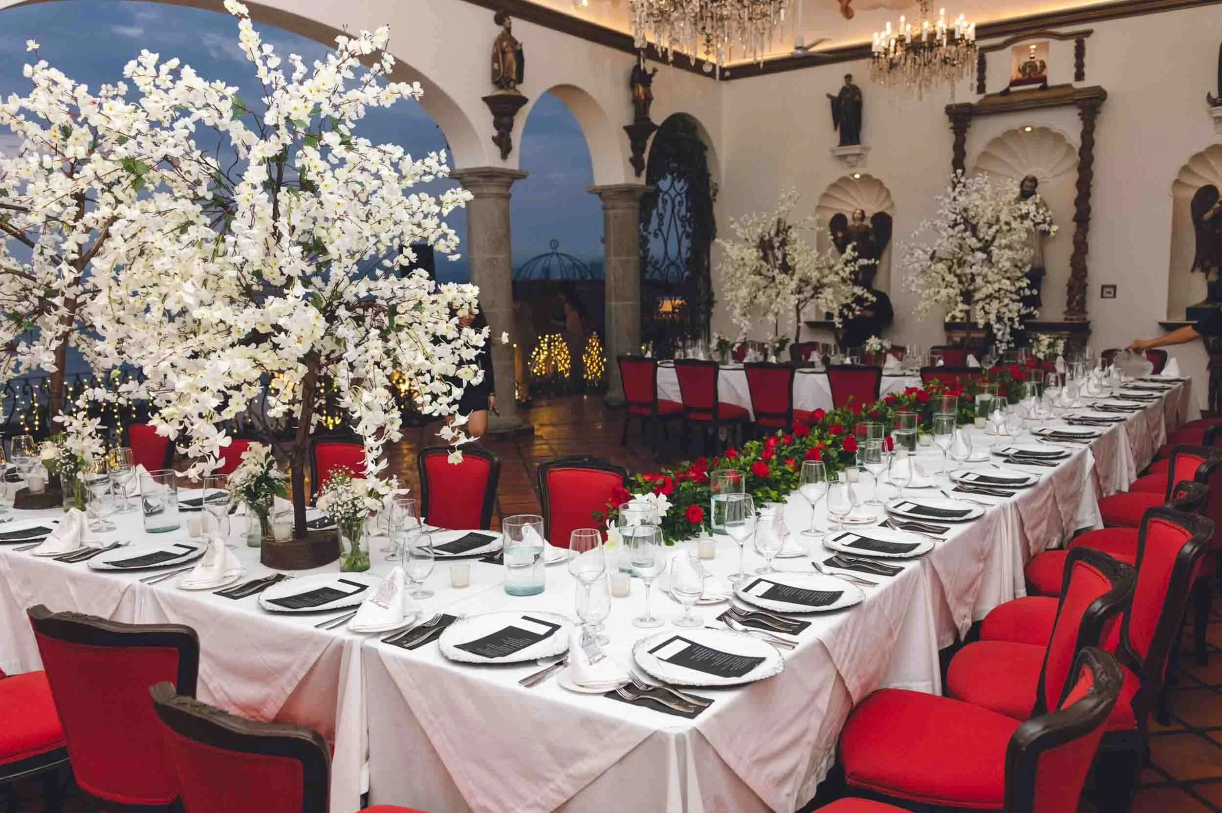 Elegant banquet hall of La Capella with round tables covered in white tablecloths, decorated with white floral centerpieces and red chairs, set for a wedding.