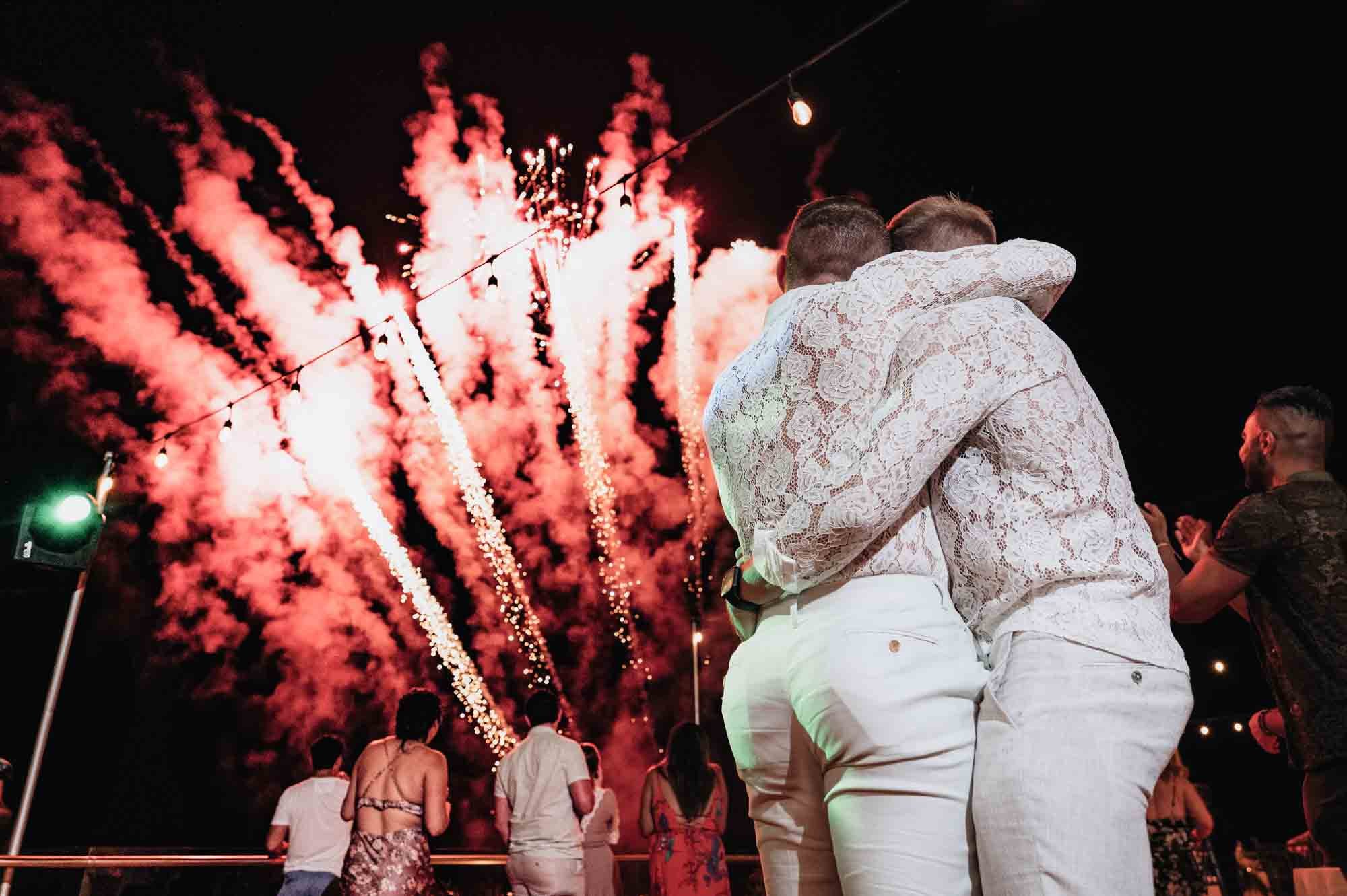 Grooms hugging watching surprise fireworks for their wedding
