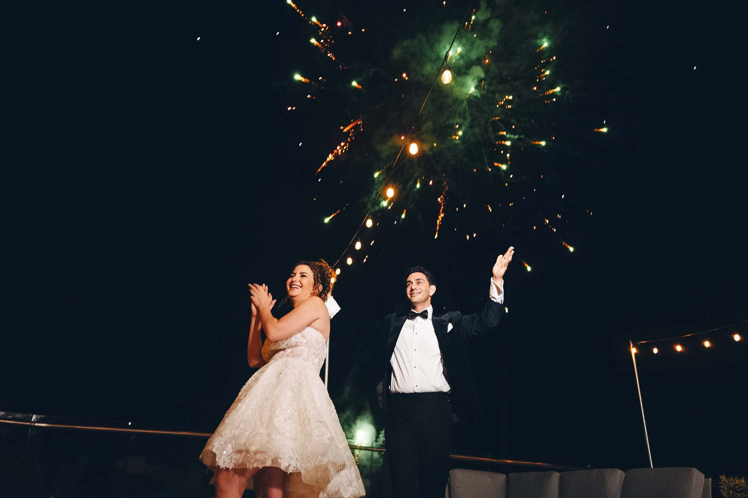 Bride and groom at their wedding celebration with fireworks in the background.