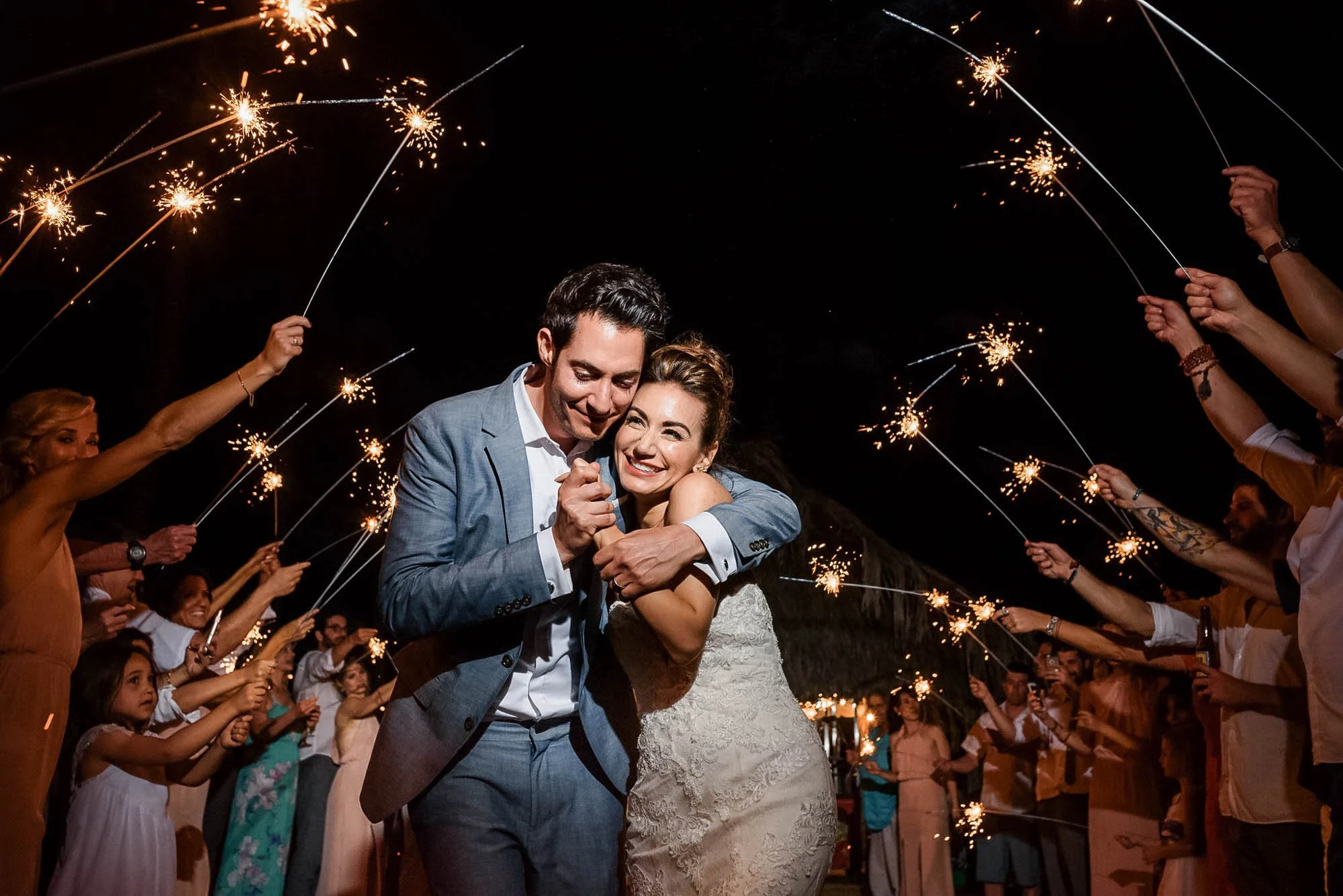 Sparkler exit at beach wedding with bride and groom hugging and smiling.