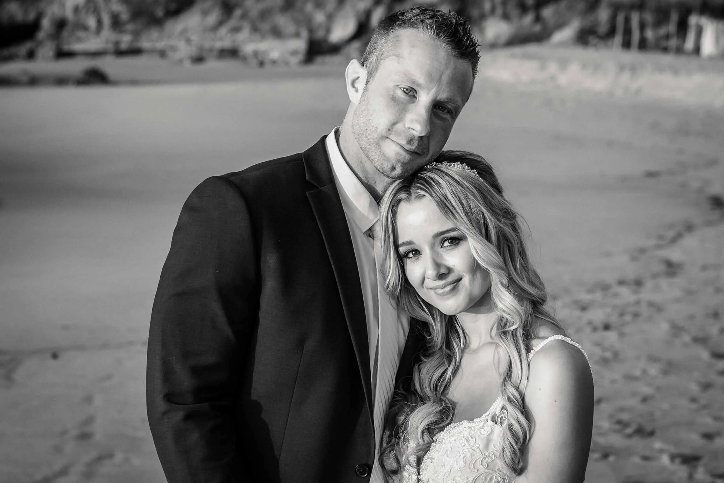 A black and white photo of a couple of newlyweds at the beach, embracing each other.
