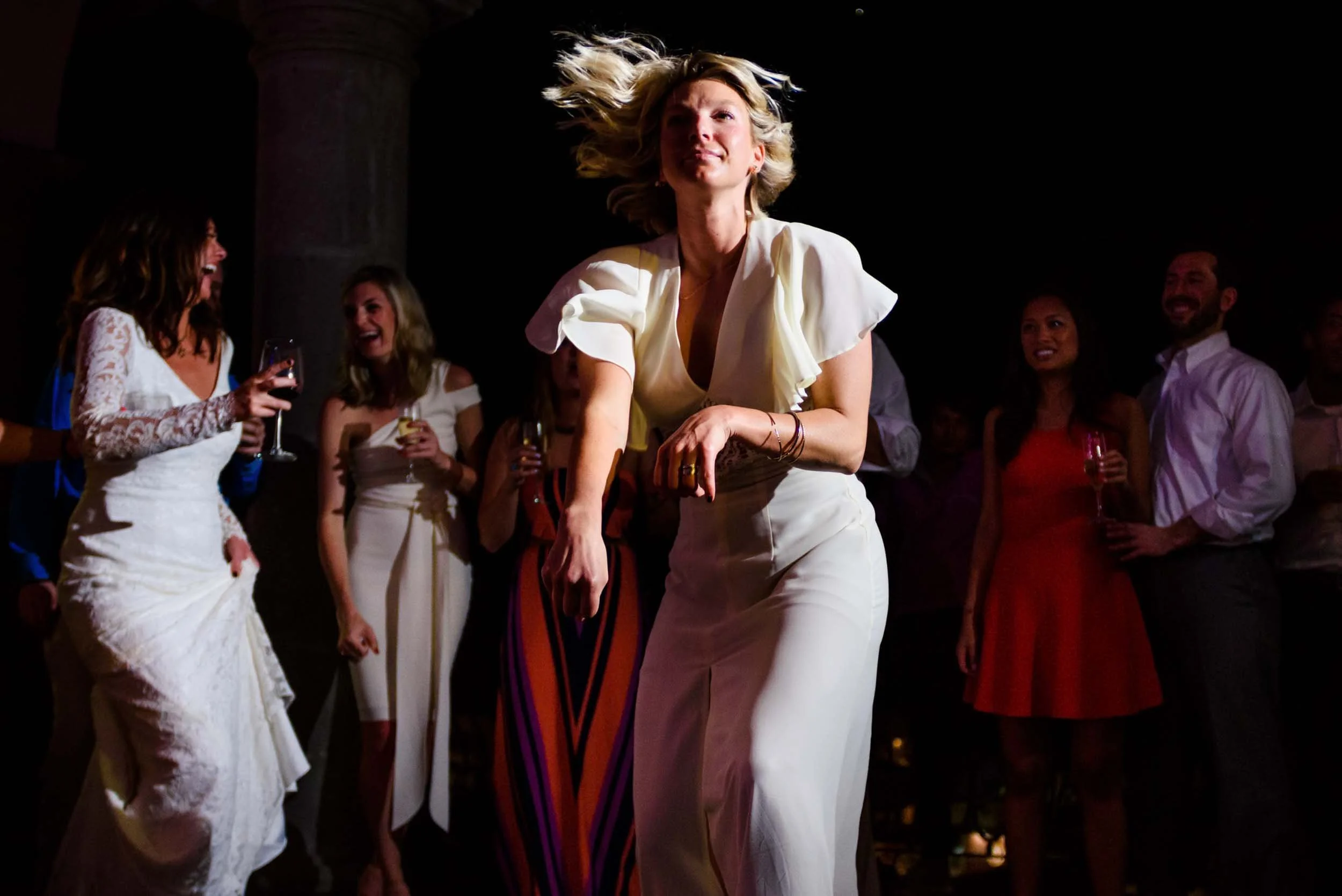 Group of people dancing and socializing at a party, with one woman in the center moving energetically.