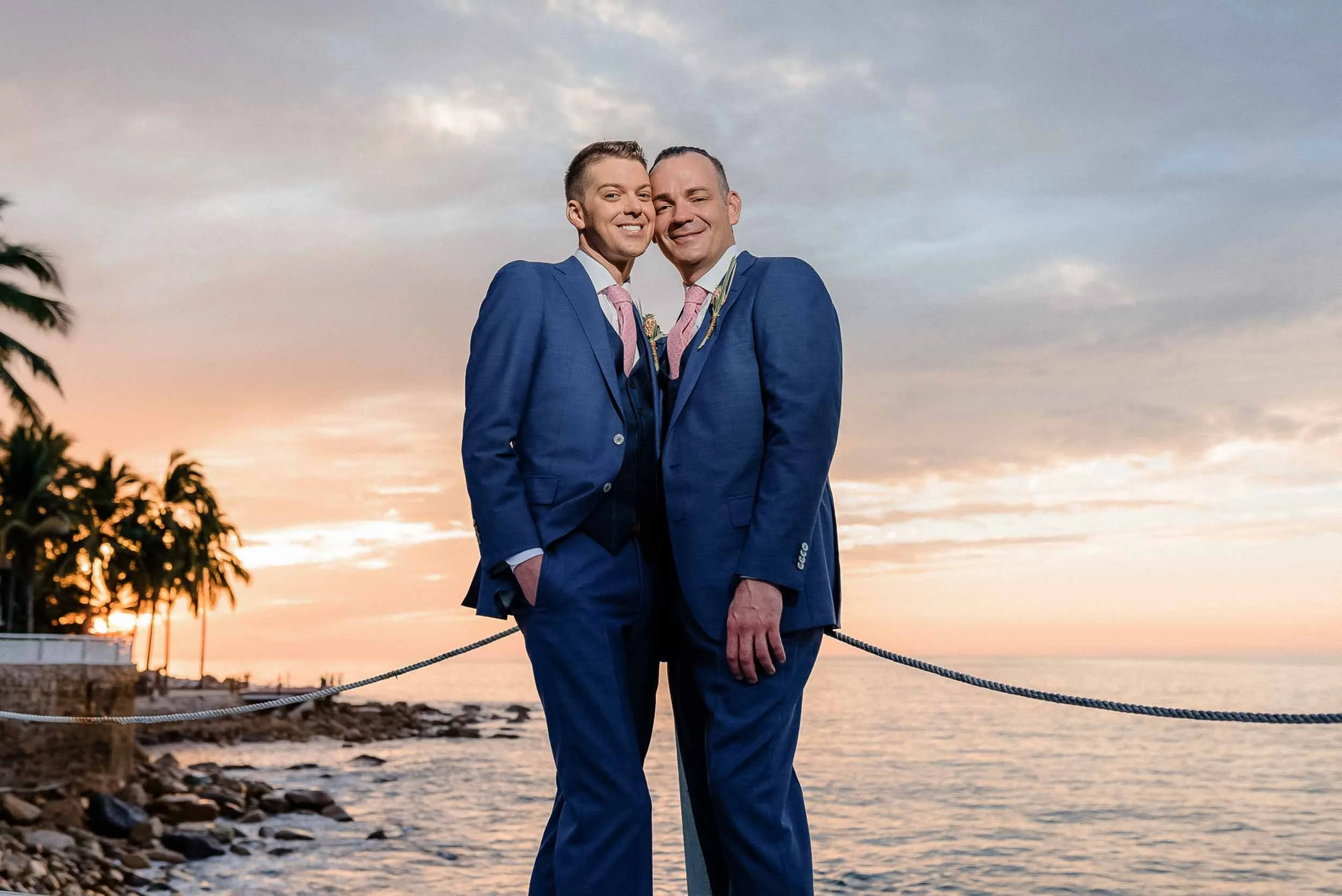 Grooms posing for portraits after their wedding ceremony in Puerto Vallarta with a sunset backdrop