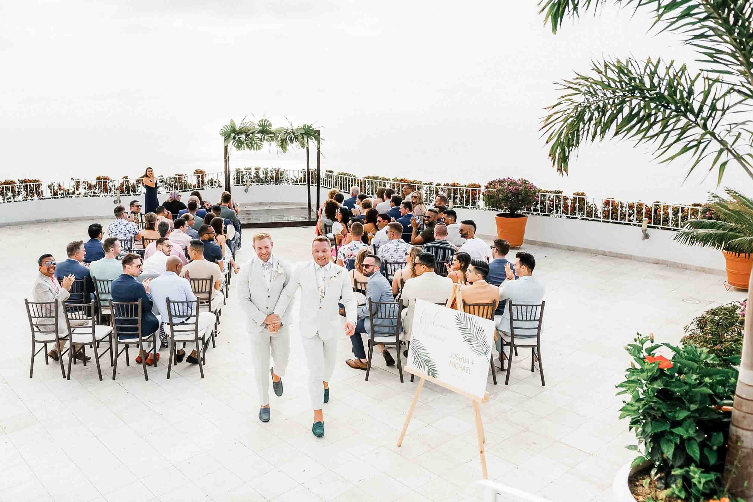 LGBTQ Wedding ceremony on a rooftop with guests seated in chairs, just as the grooms exited their wedding ceremony at the Grand Miramar resort. 