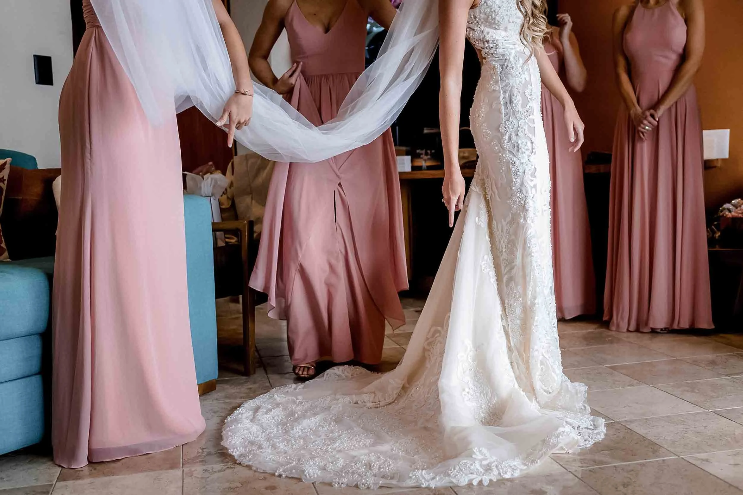 Bridesmaids in pink dresses surrounding a bride in a white wedding gown during their final touches before the ceremony.