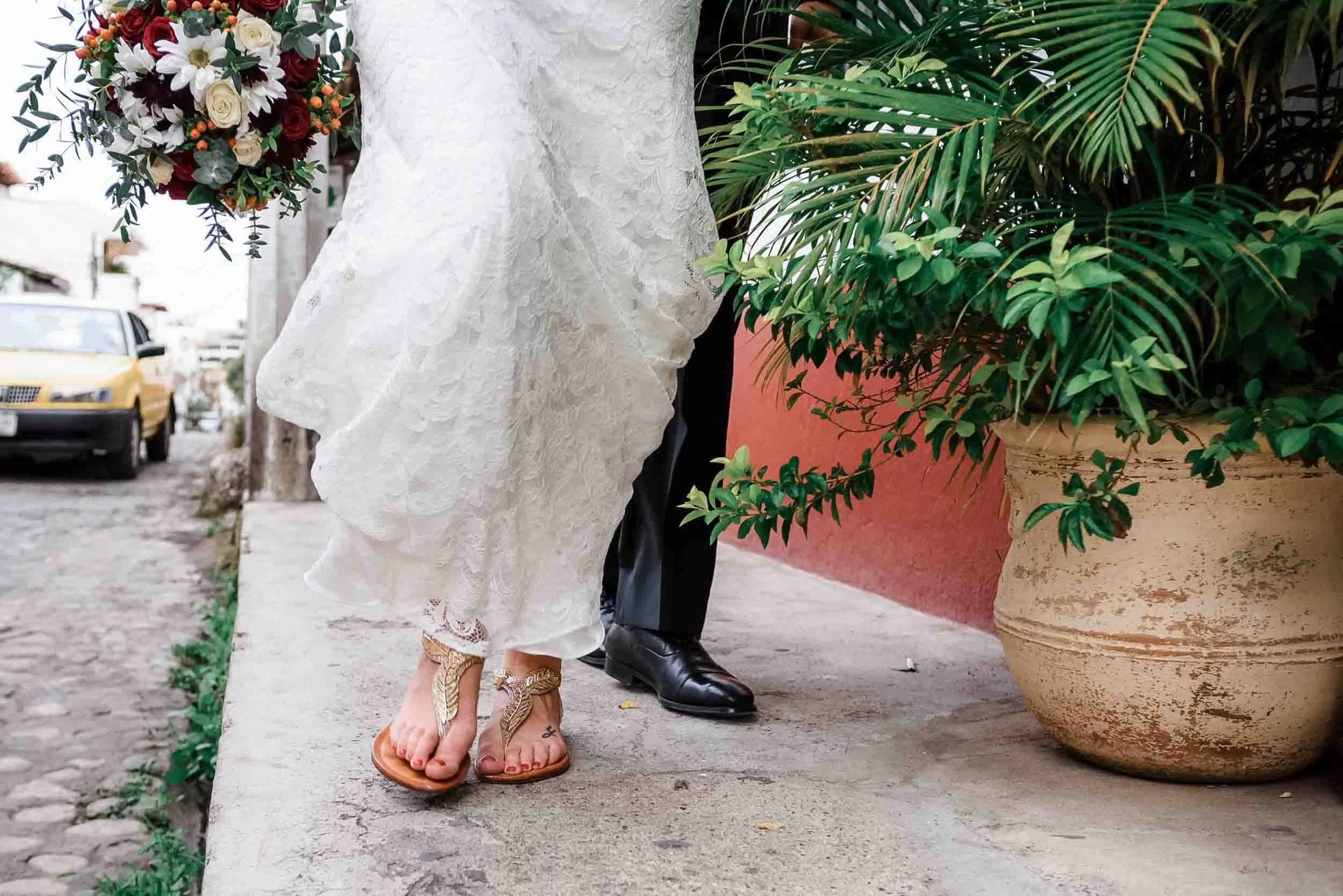 Close-up of the lower halves of bride and groom walking on sidewalk of downtown Puerto Vallarta, bride is holding her flower bouquet.