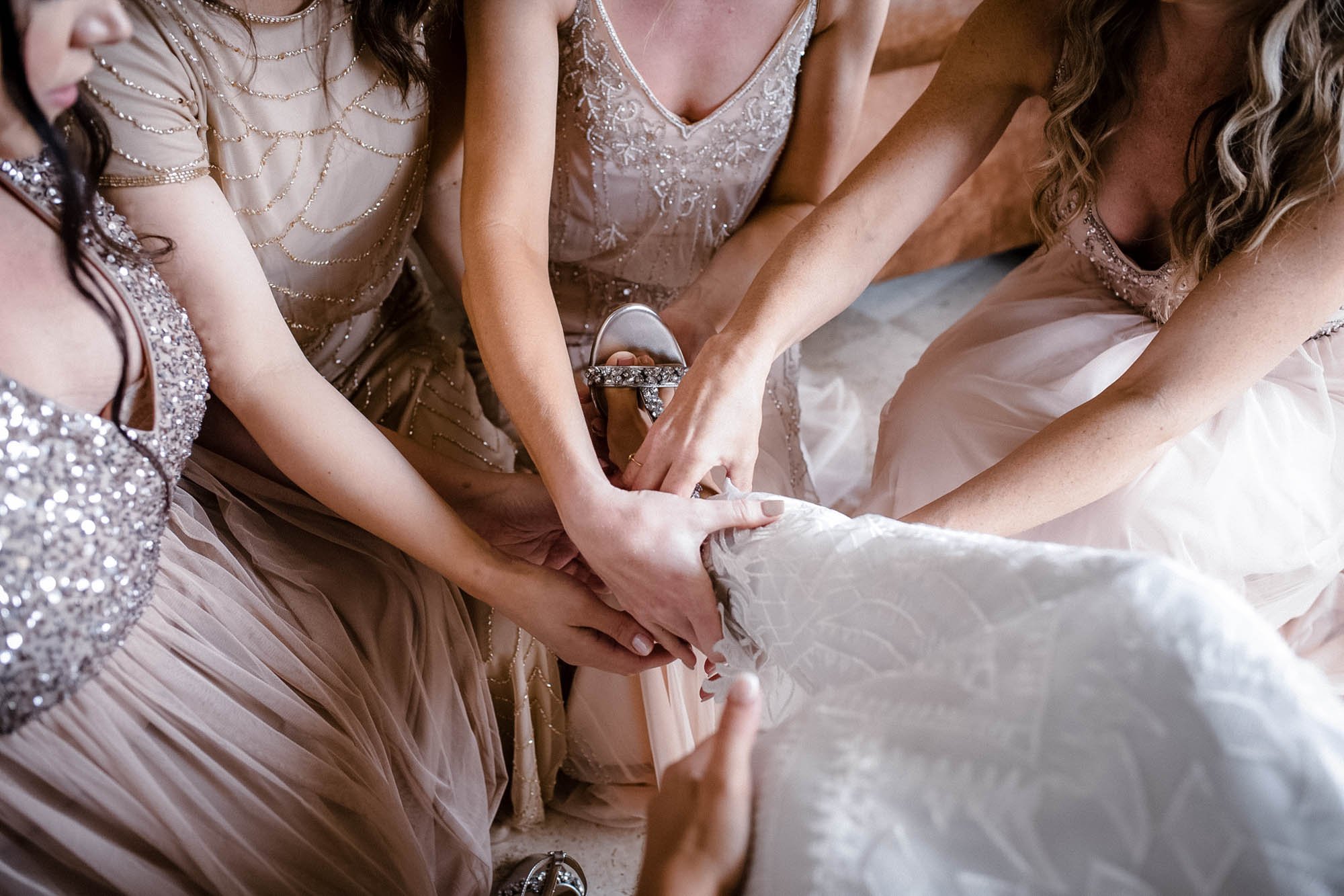 Bride and bridesmaids during their getting ready putting the shoes on the bride before wedding ceremony.