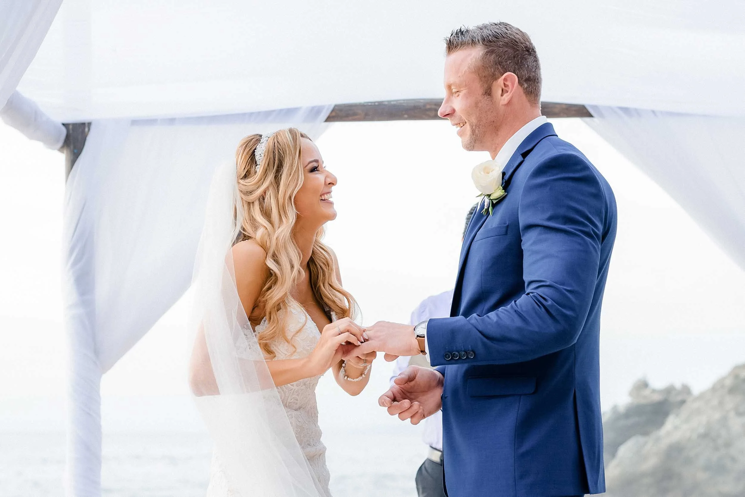 A bride and groom holding hands and smiling at each other during their beach wedding.