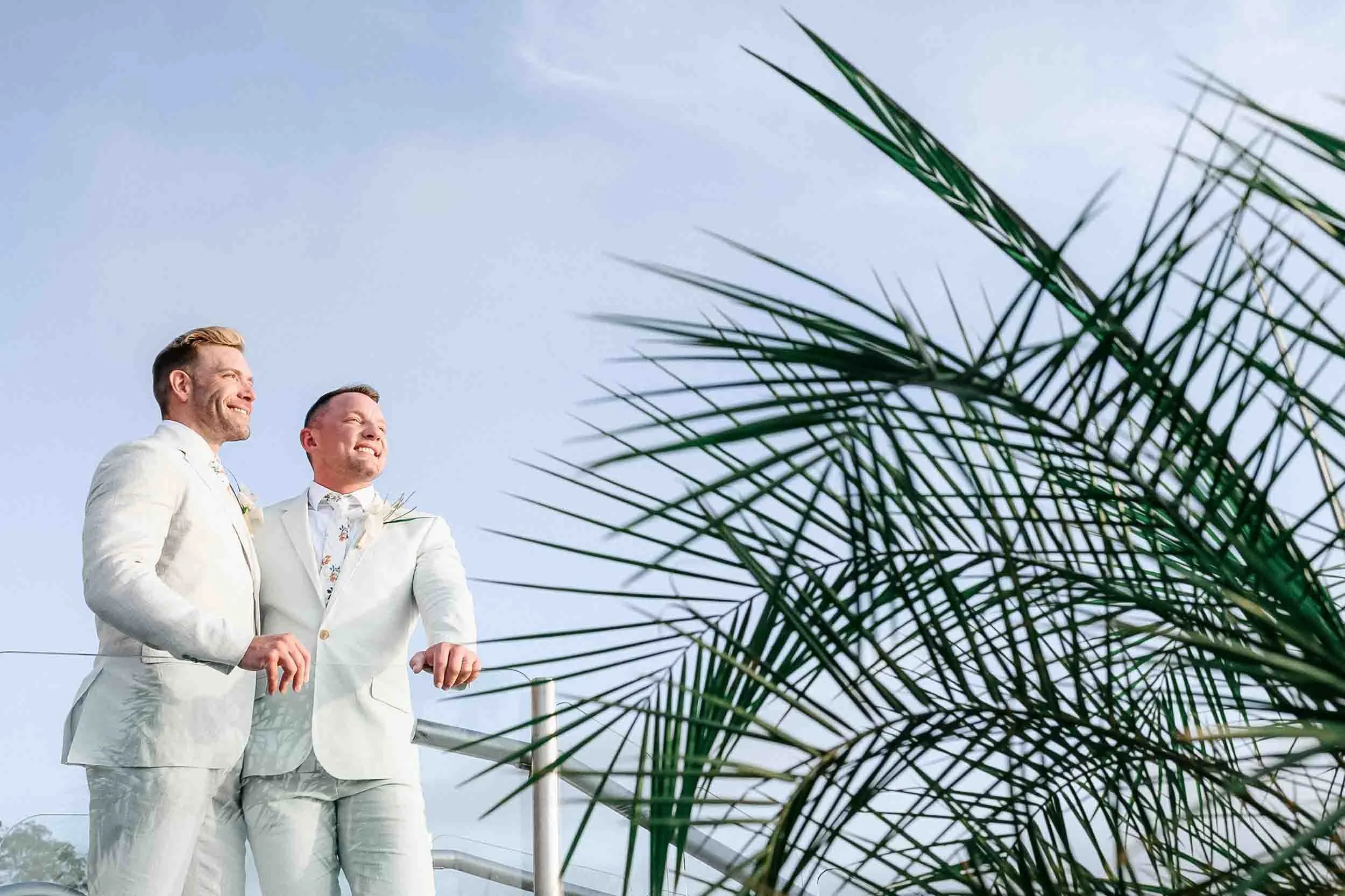 Portrait of lgbtq couple with their wedding attire after their destination wedding, and a blue sky background. 