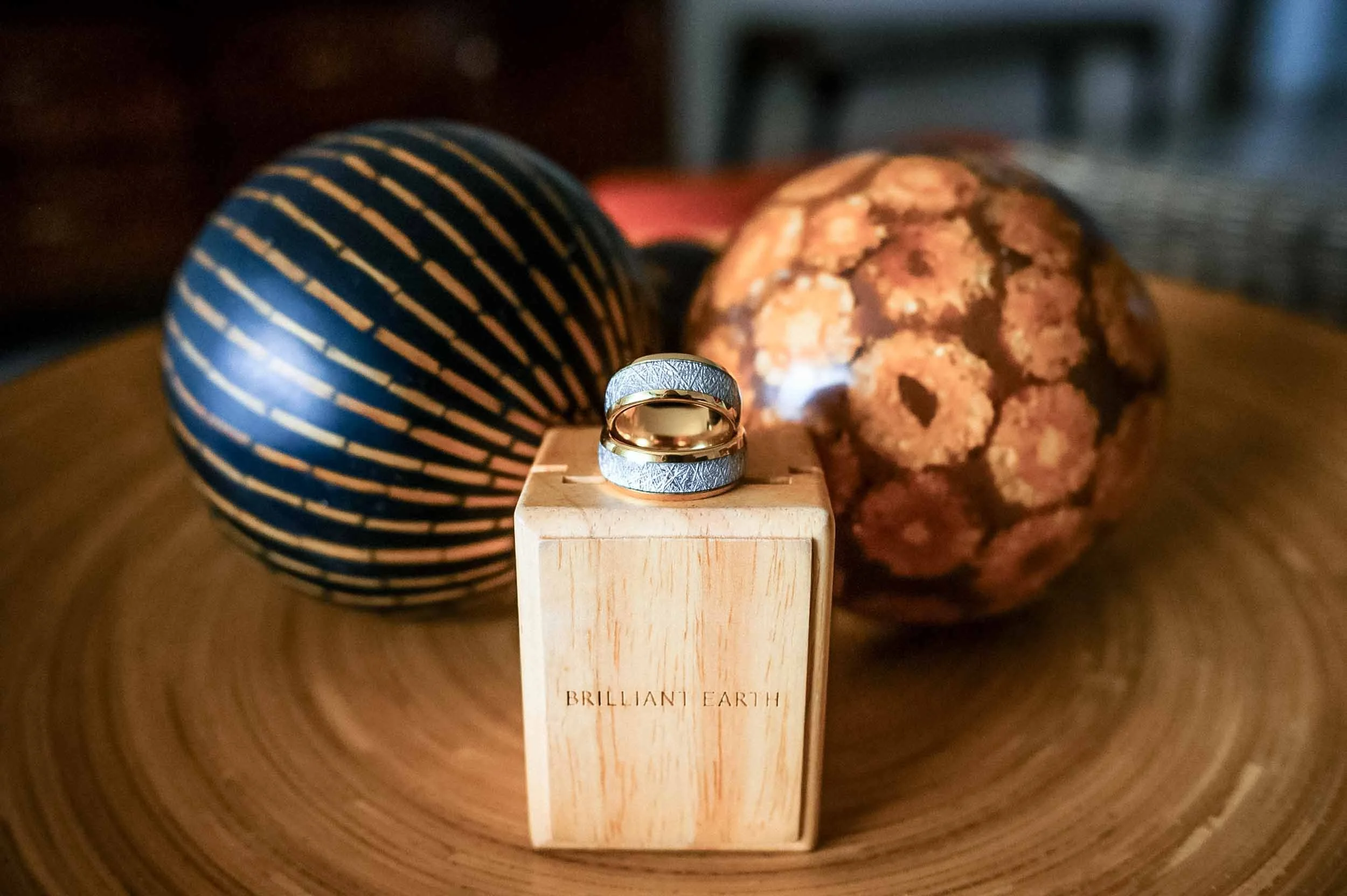 A wooden block with the words 'Brilliant Earth' engraved, holding wedding rings with intricate patterns.