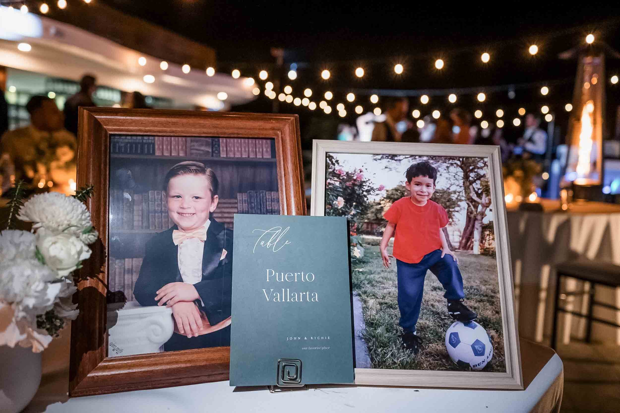 Photographs of two young boys who are the grooms when they were little, one dressed in formal attire and the other in casual sportswear, displayed on a table at their wedding.