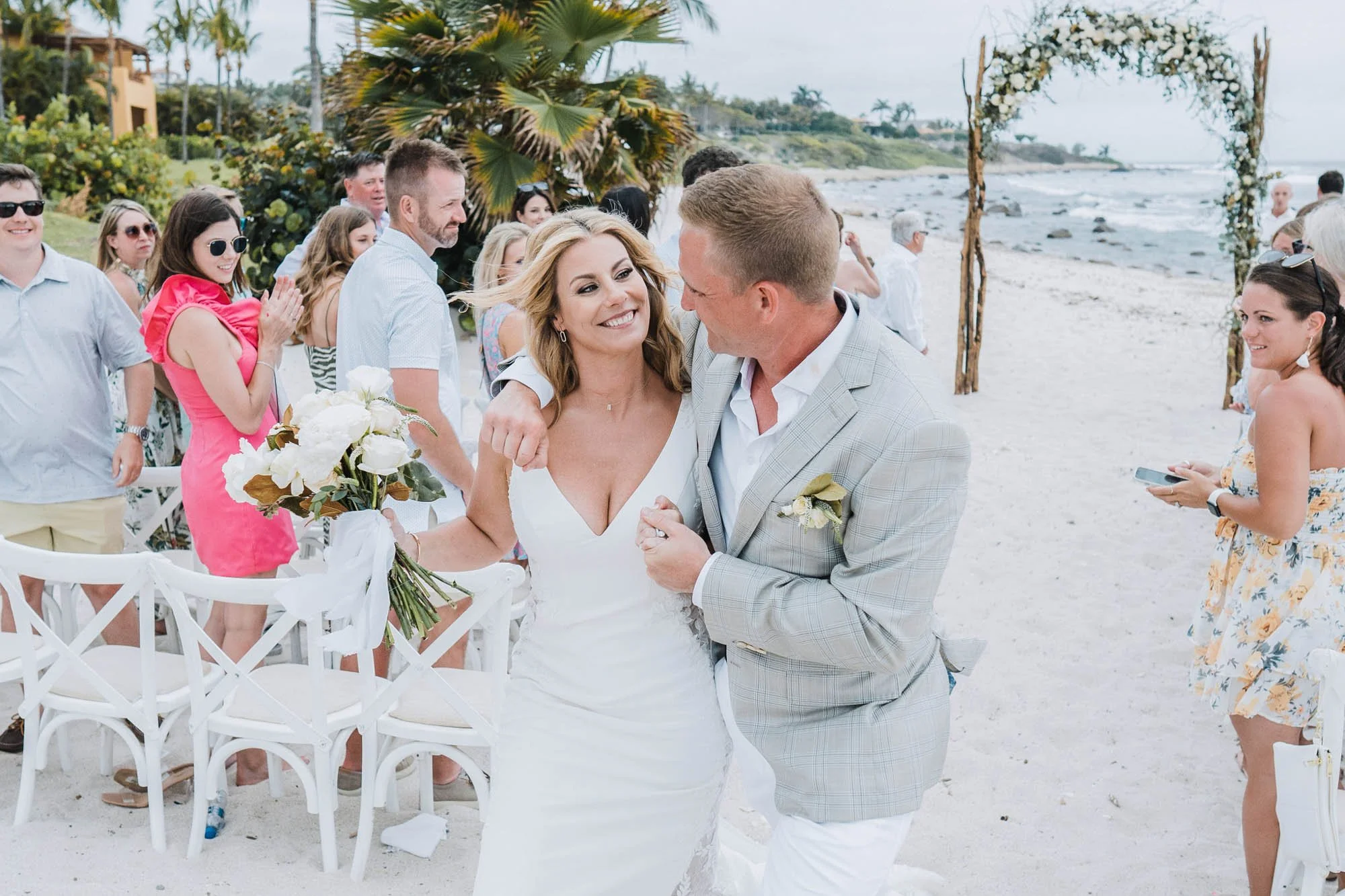 Bride and groom exiting beach ceremony hugging each other.