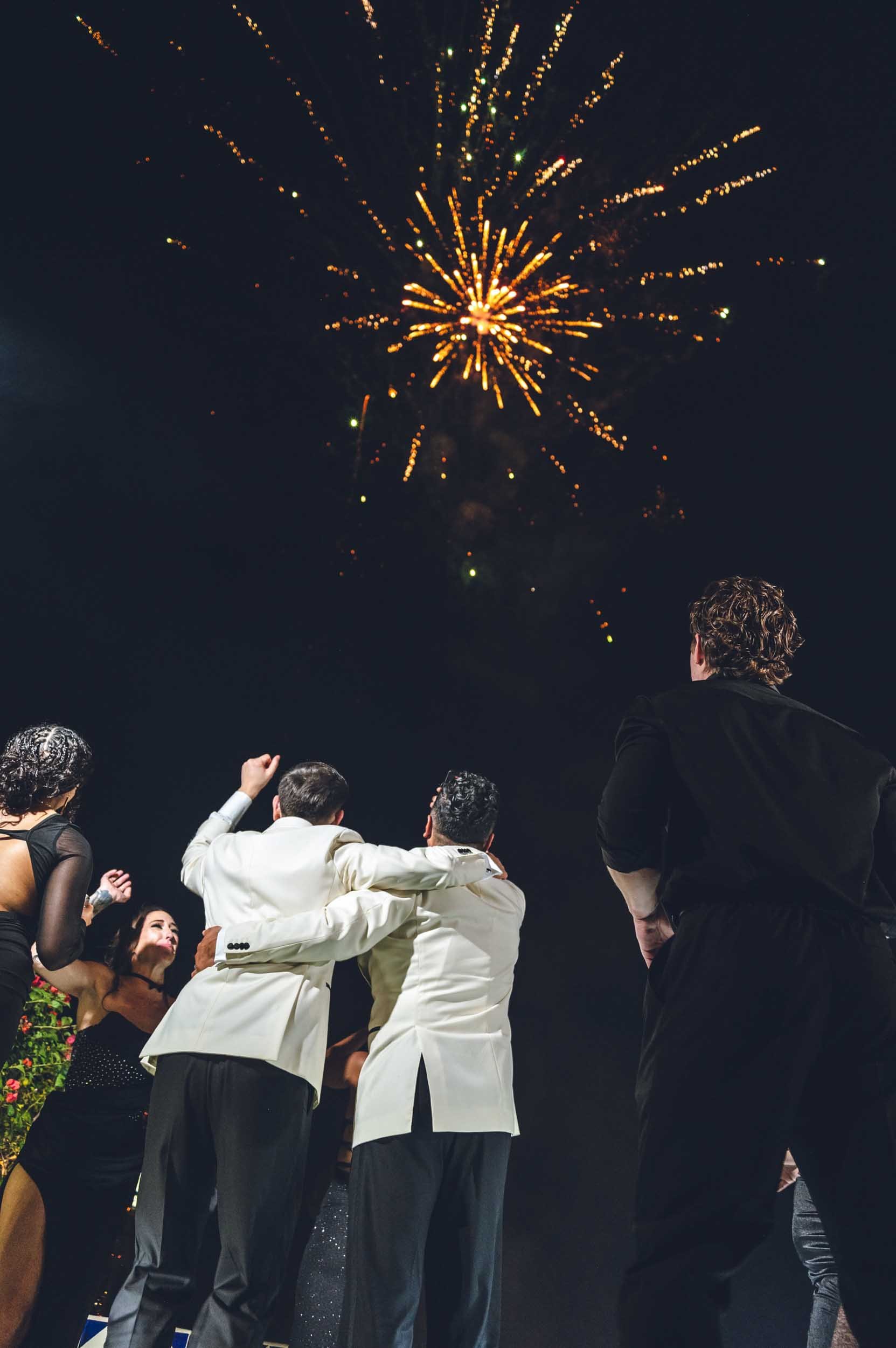 Grooms cheering while the watch their wedding fireworks in the night sky.