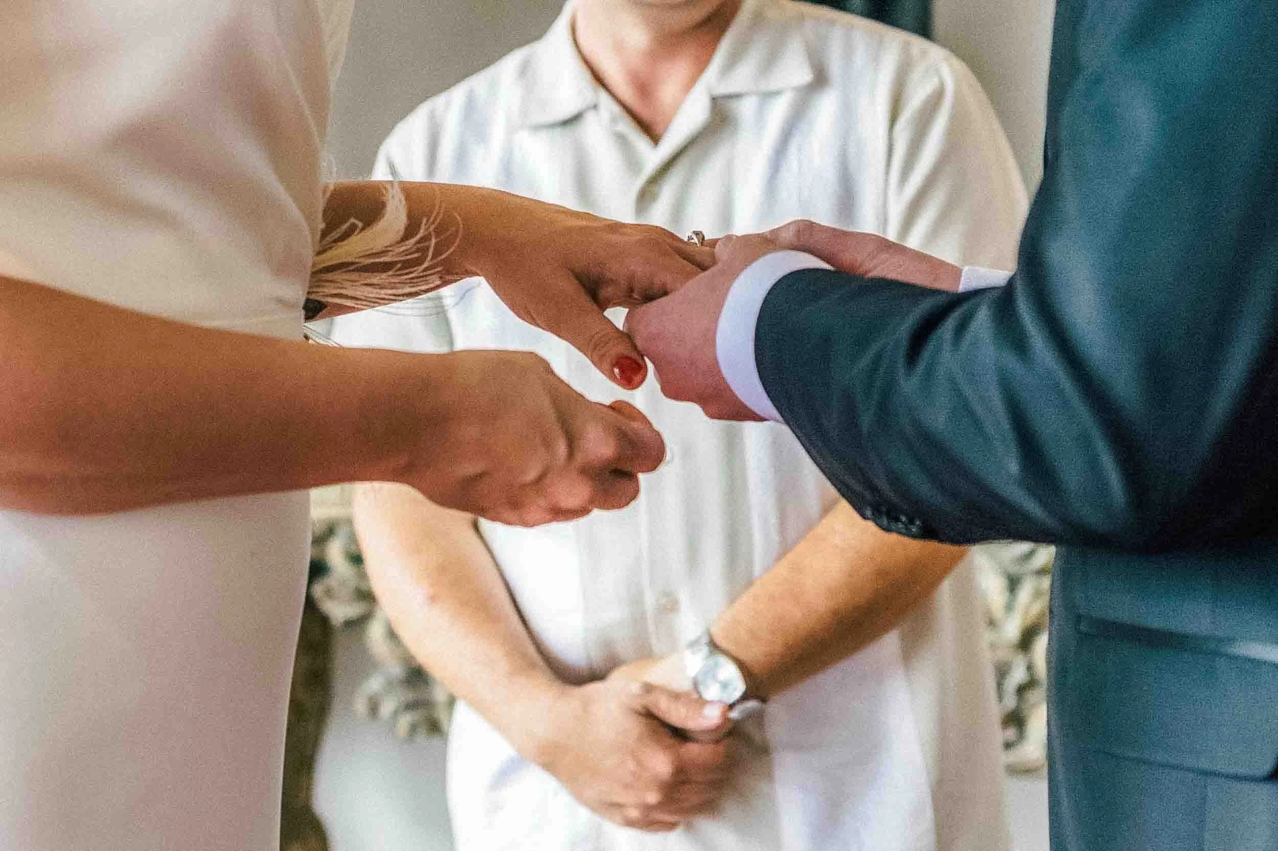 Bride and groom, groom is placing ring on the hand of the bride during their wedding ceremony.