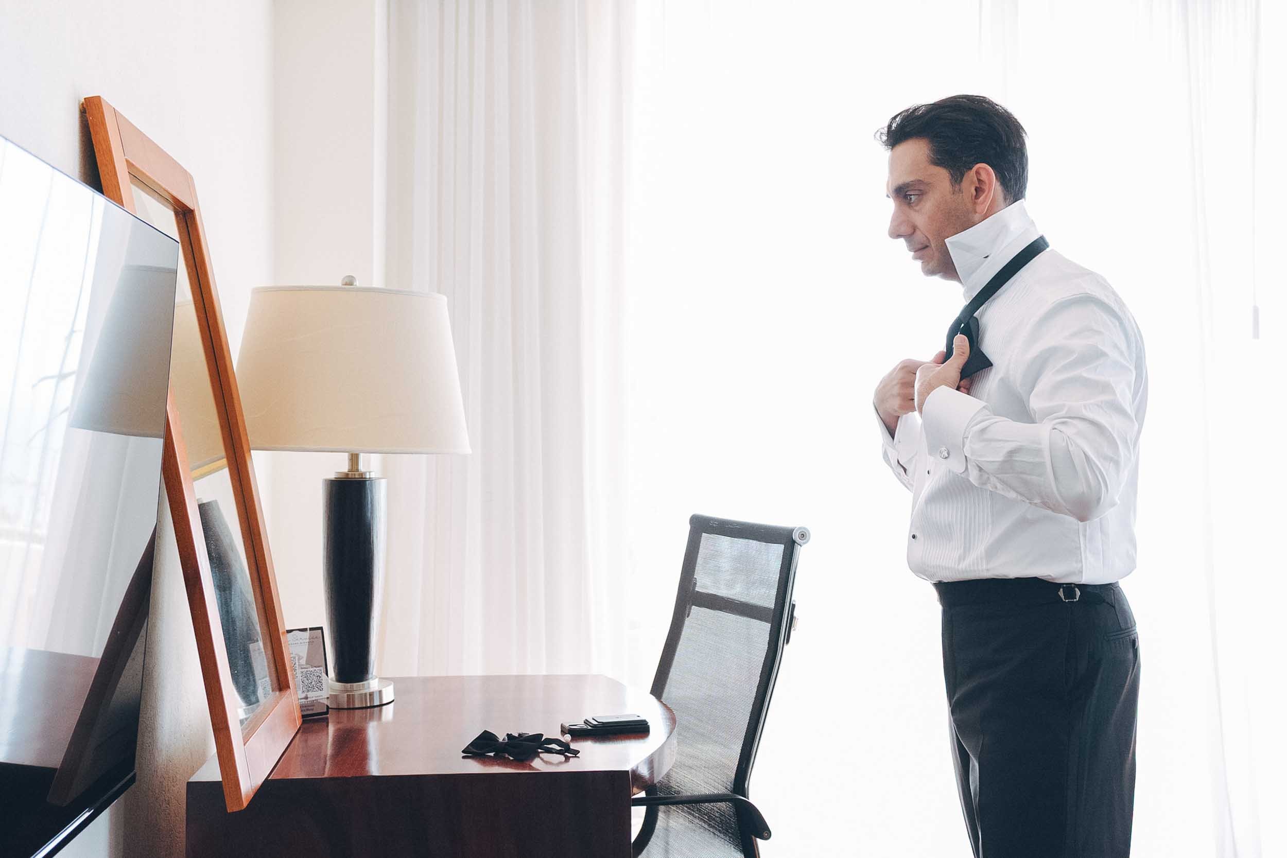 Groom getting ready, fixing his bow tie before leaving to the wedding ceremony.