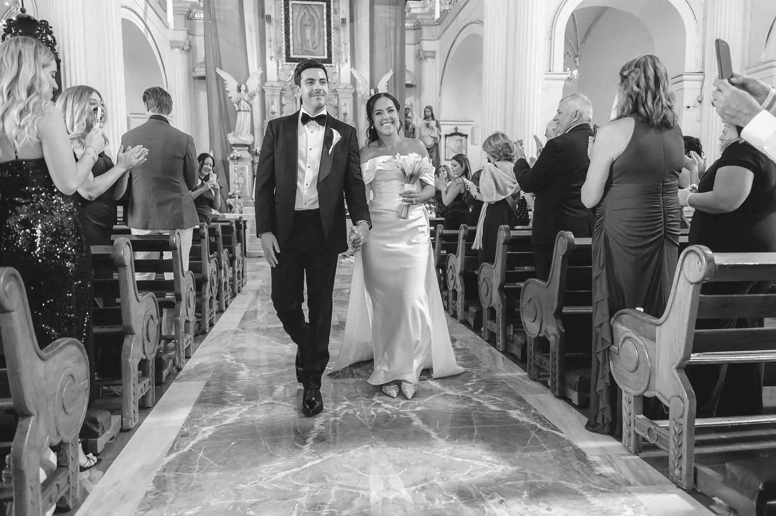 A bride and groom walking hand in hand down the aisle of a church surrounded by friends and family celebrating their wedding.