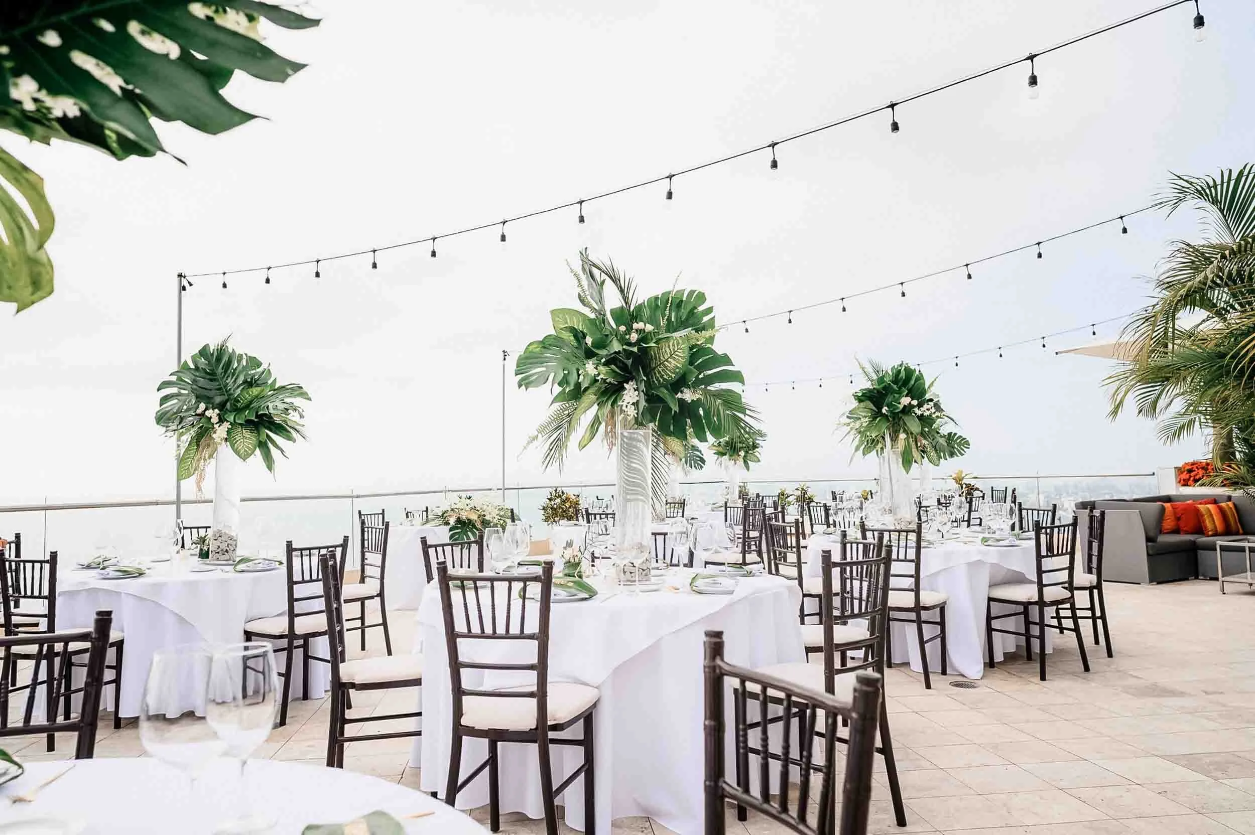 Wedding reception area and setting with white color prevailing and greenery accents in each table. 