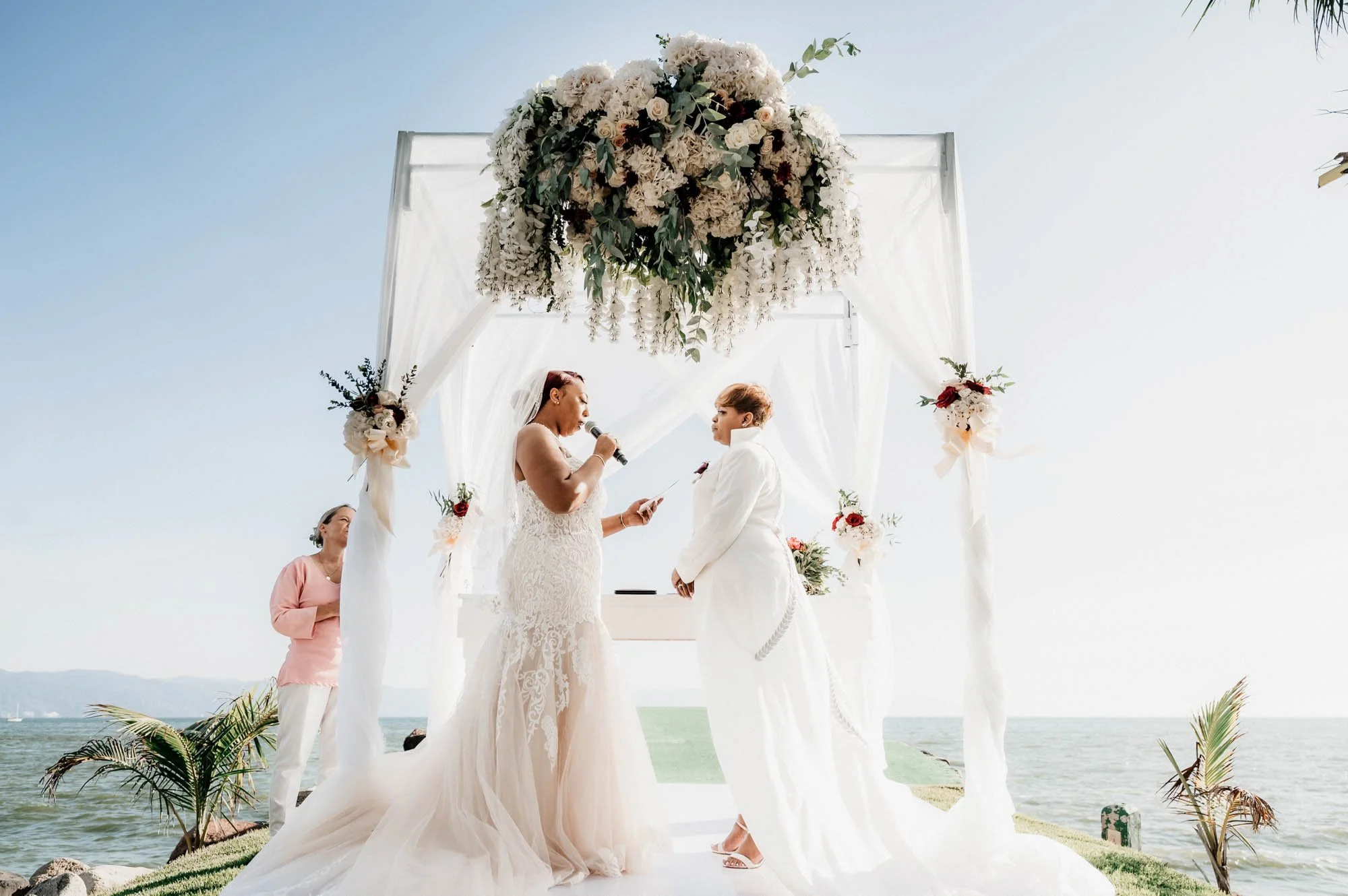 LGBTQ brides during their vow exchange on their wedding day with a beach backdrop.