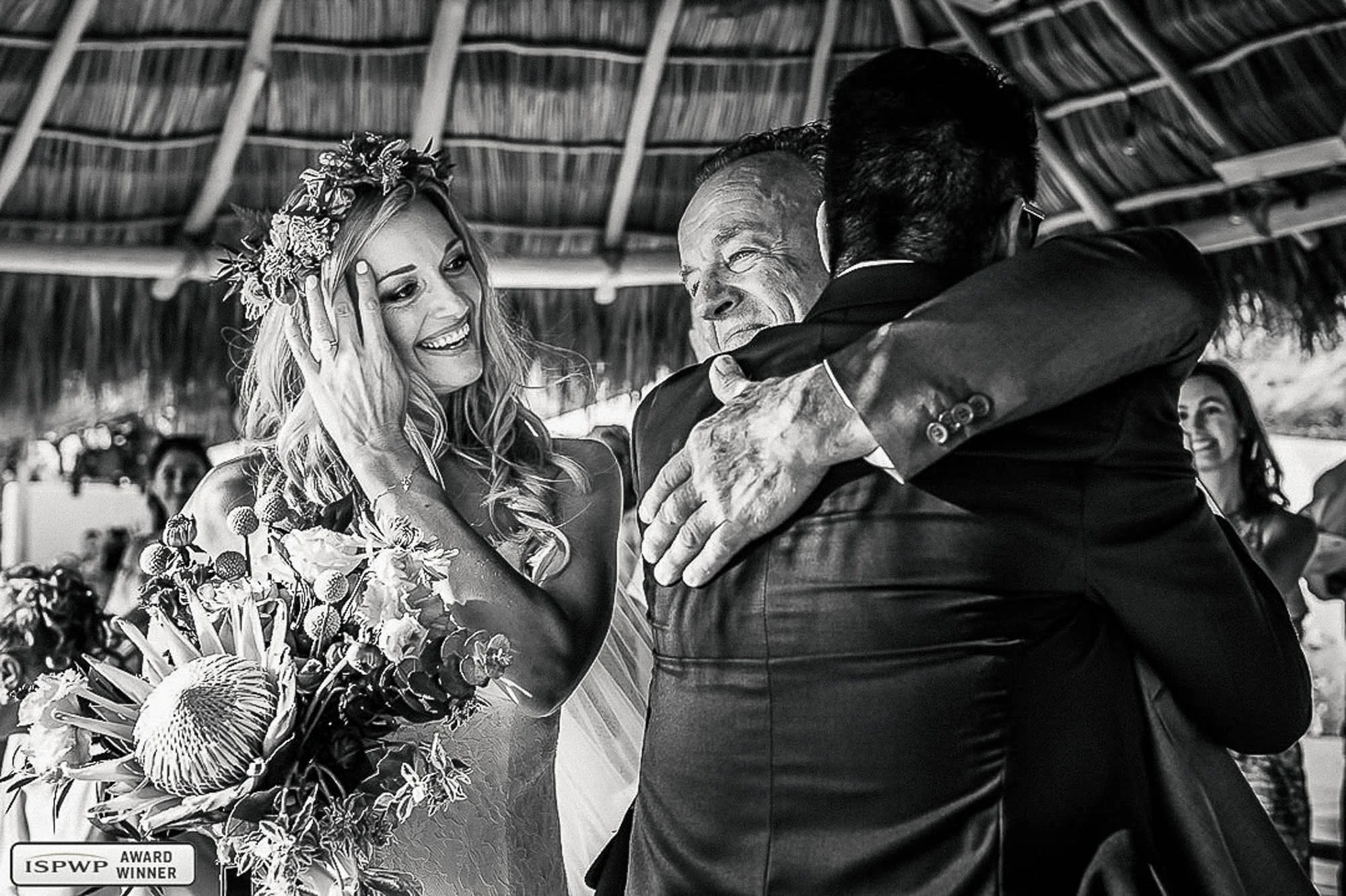 Bride smiles while her father hugs the groom after walking her down the aisle. 