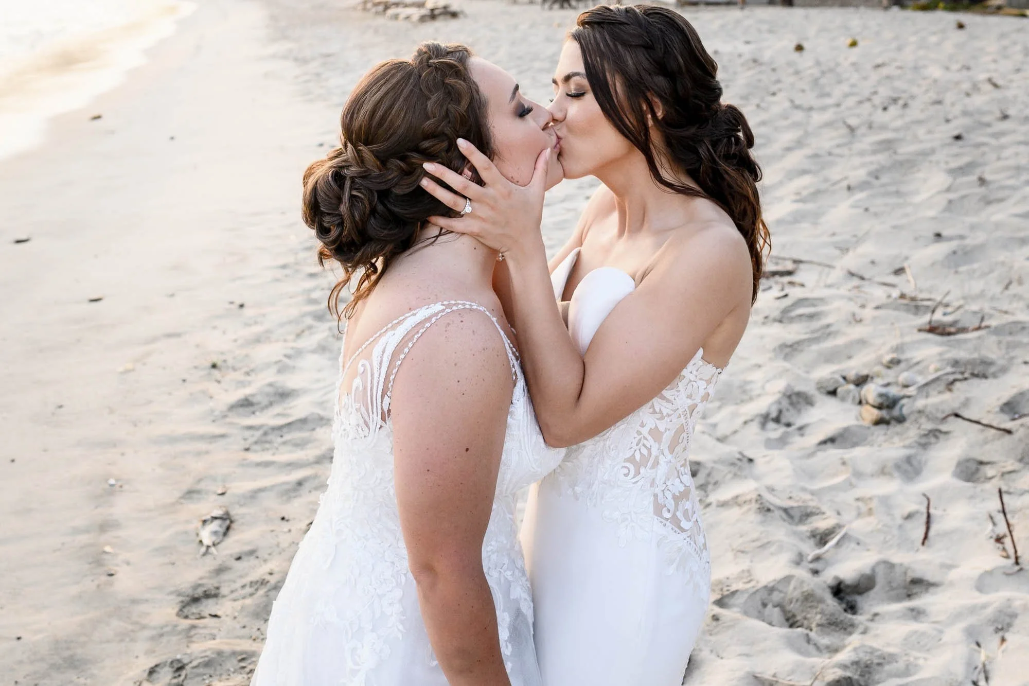 Two brides sharing a kiss during their beach wedding celebration.