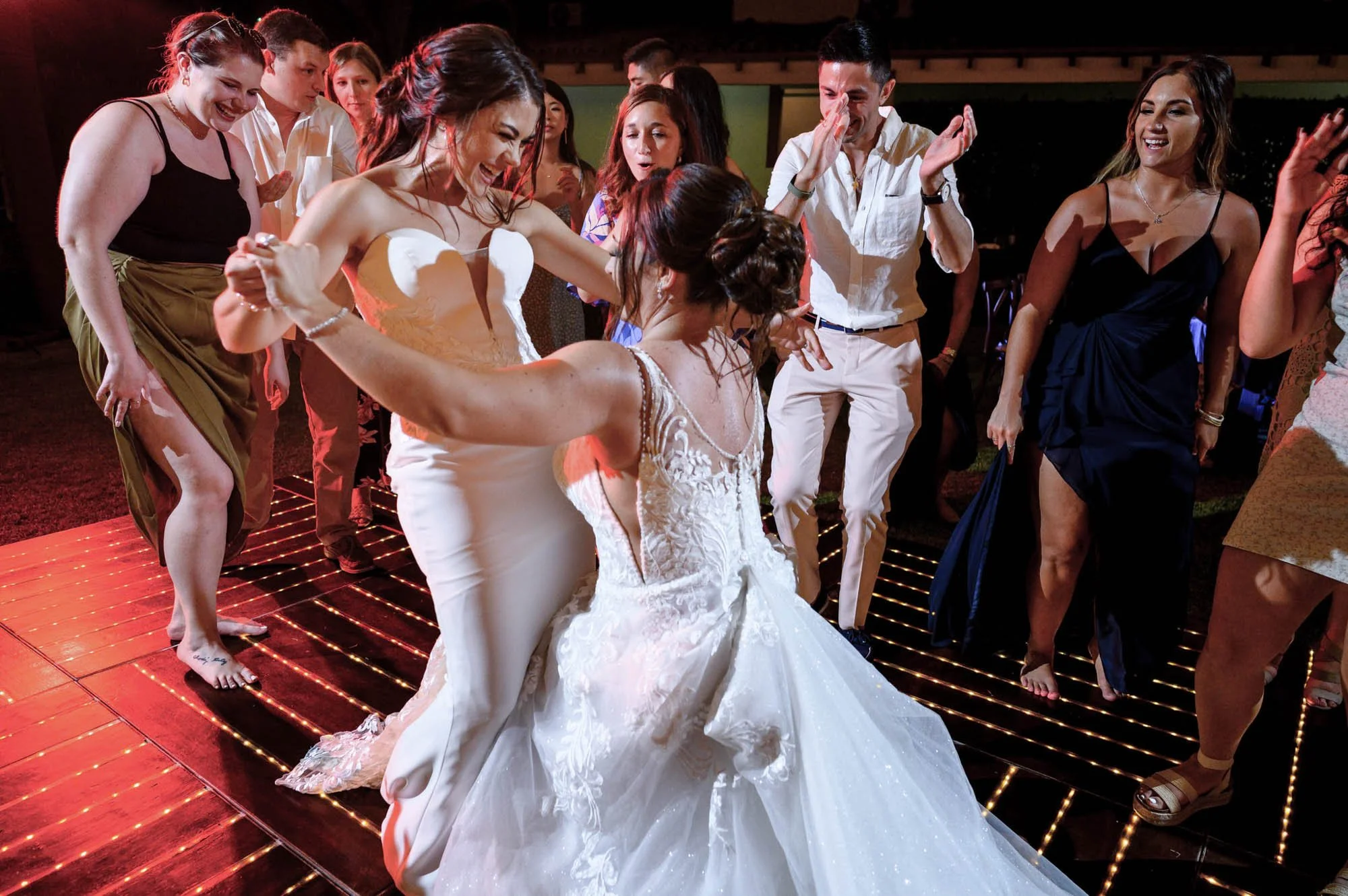 Lesbian brides having fun dancing during their destination wedding reception, and guest in the background cheering. 