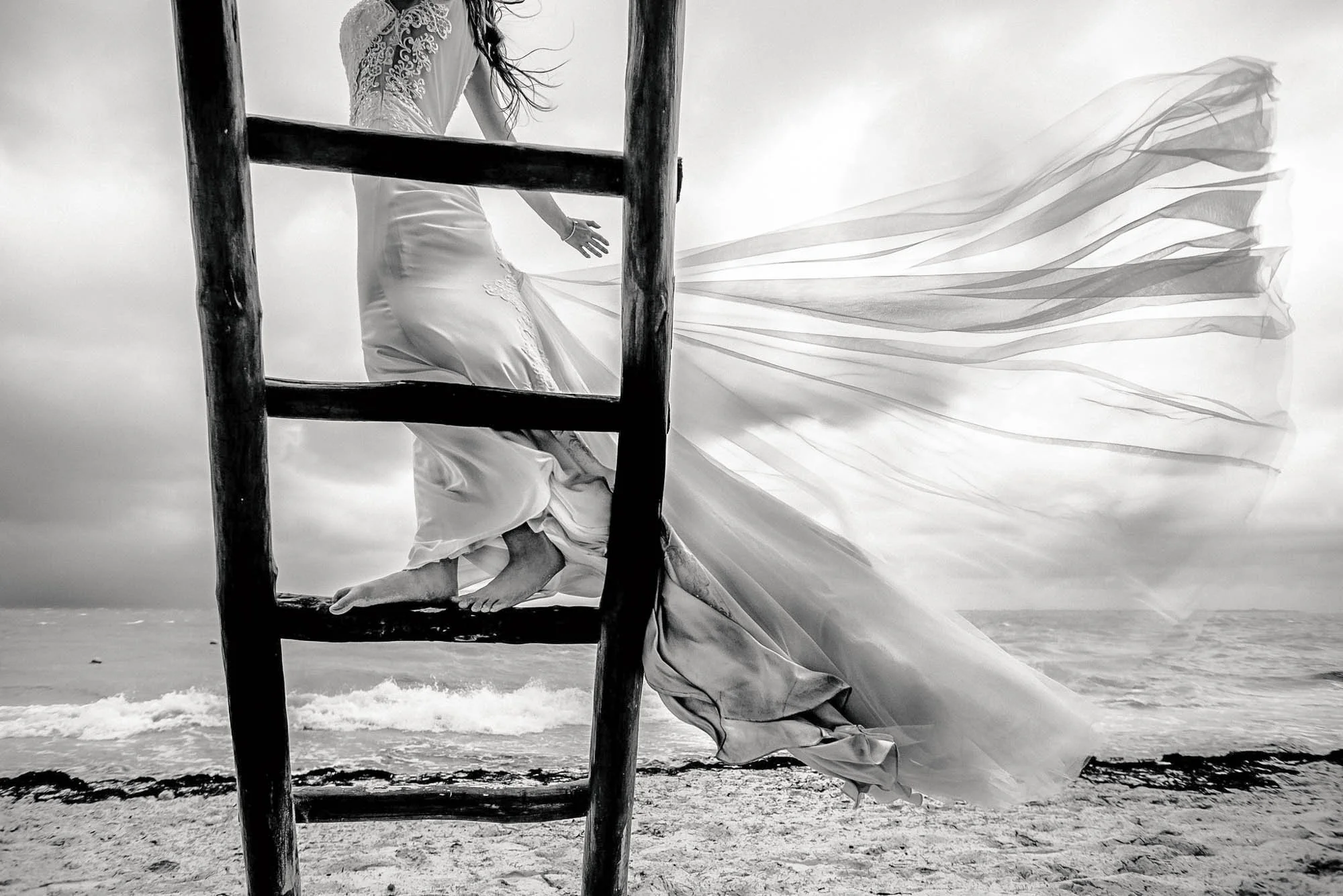 Flying wedding dress train from the strong winds at the beach with the ocean in the background.