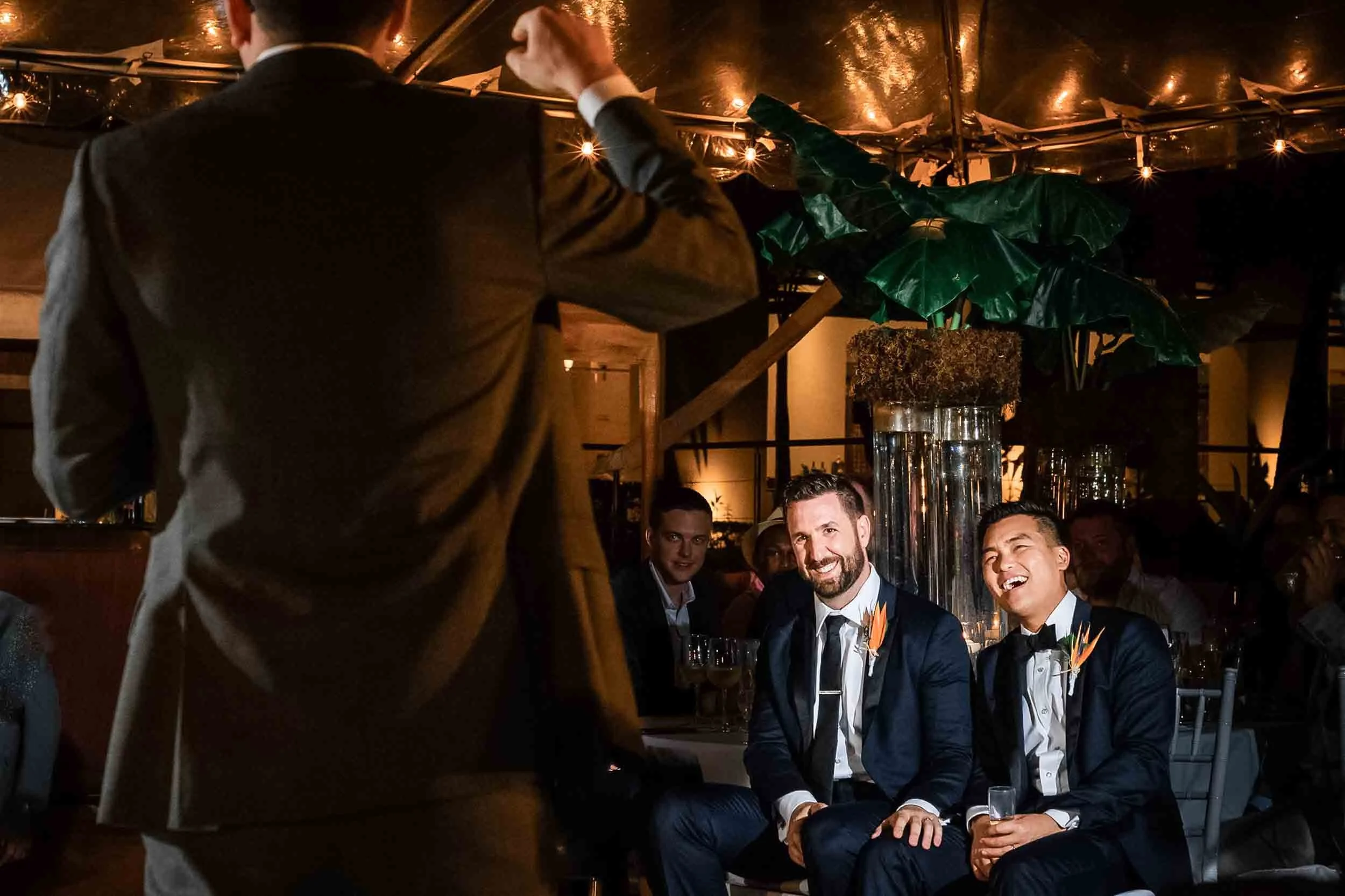 Grooms laughing during speeches given at the reception of their beach wedding.