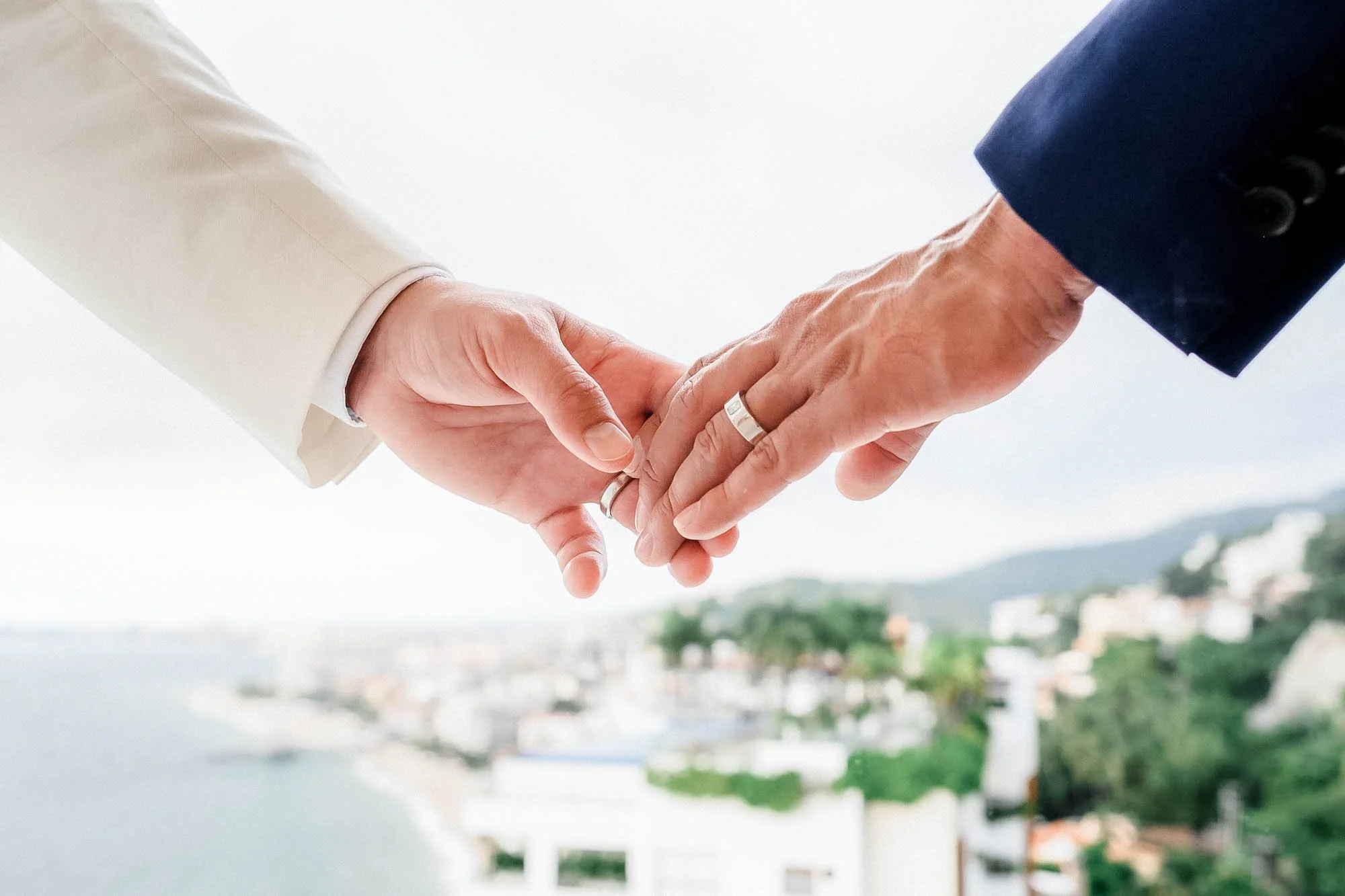 Detail of gay couple holding hands showing their wedding rings.