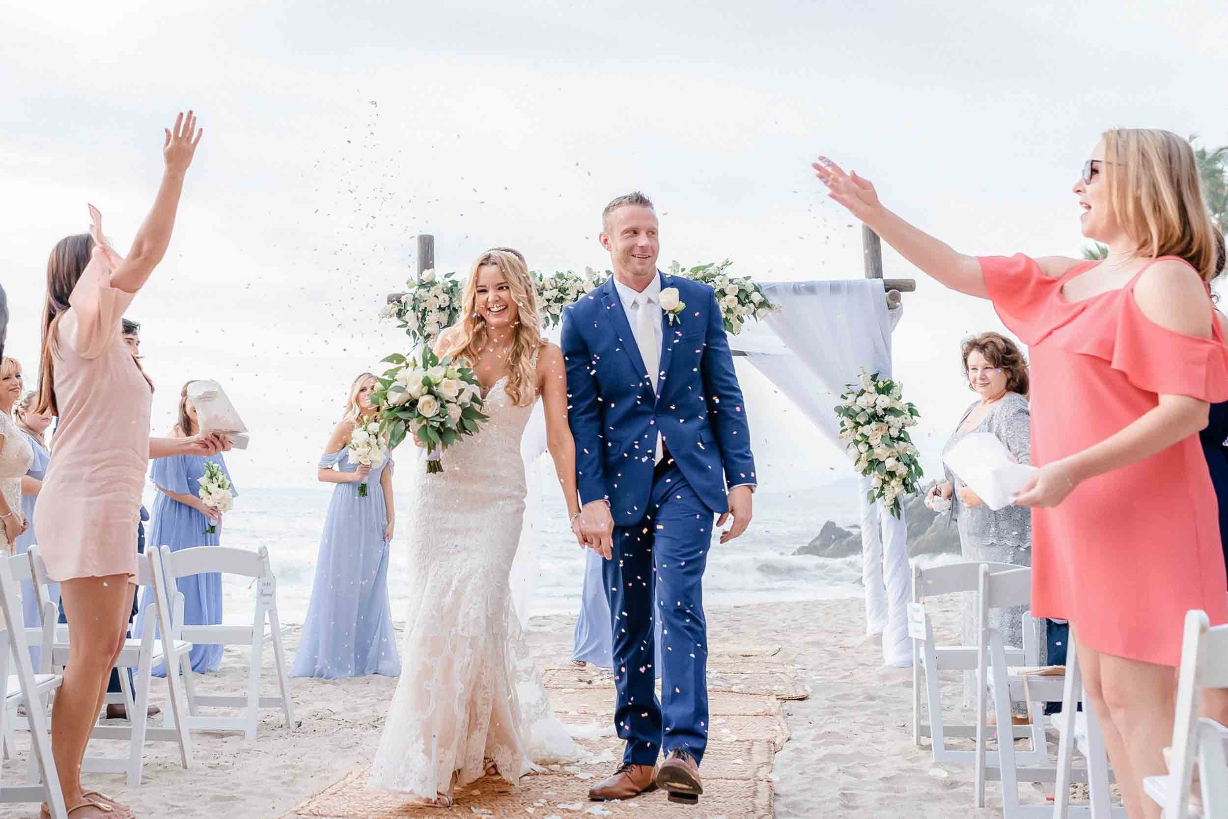 A bride and groom walking hand-in-hand during the recessional of their wedding ceremony encountering guests throwing confetti in the air at the Hyatt Ziva in Puerto Vallarta.