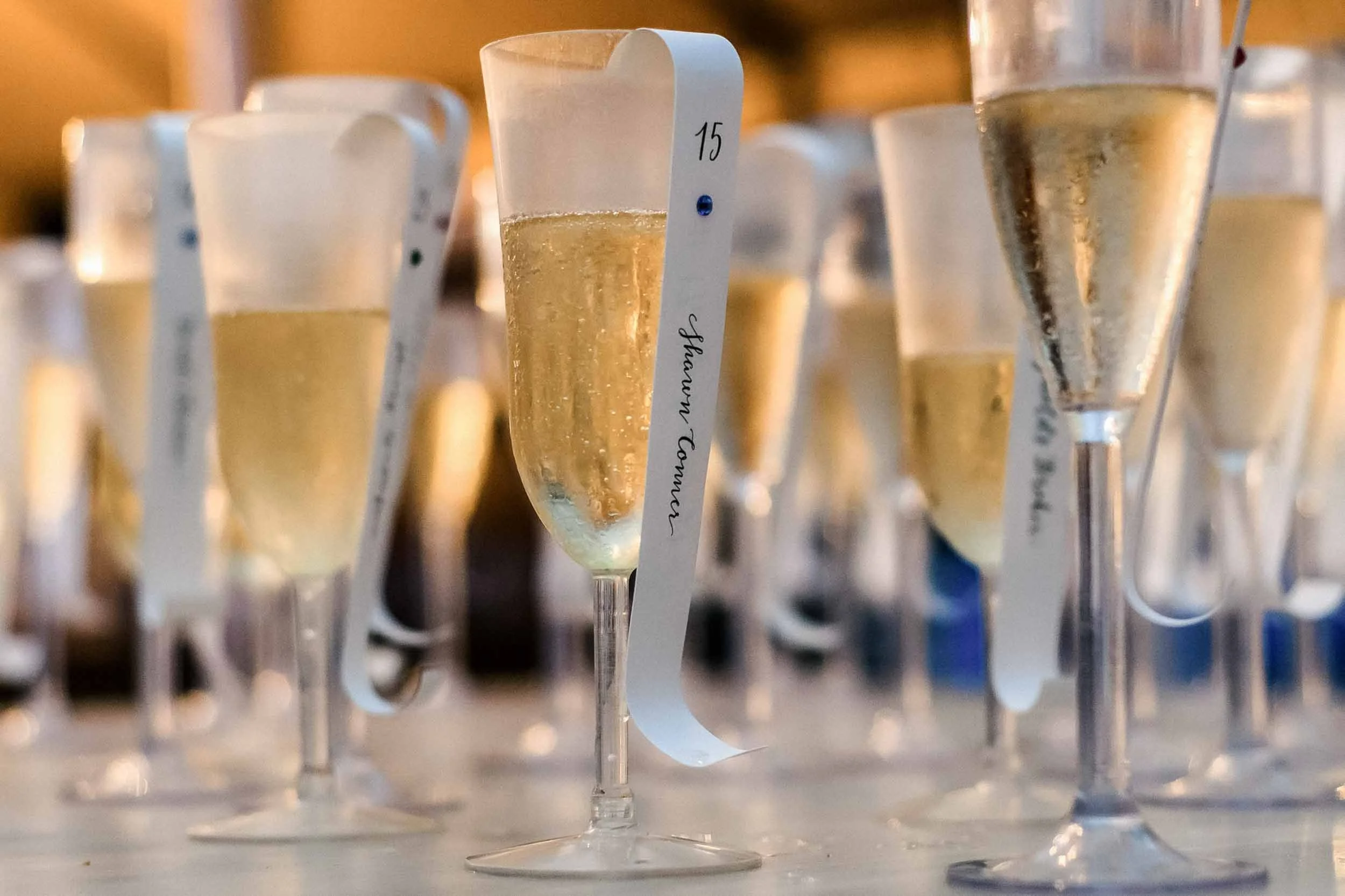 Close-up of several champagne flutes filled with sparkling wine, and papers serving as table assignments.