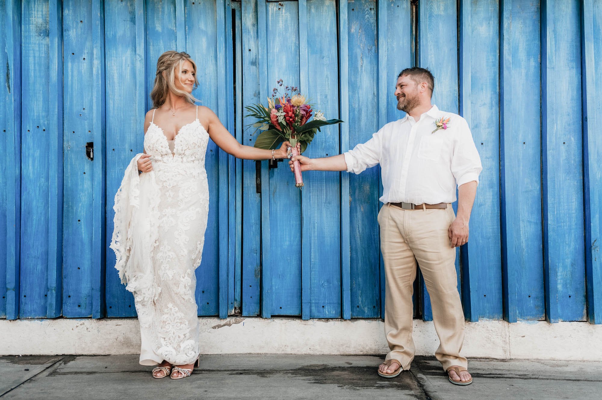 Bride and groom portrait holding flower bouquet and a blue background.