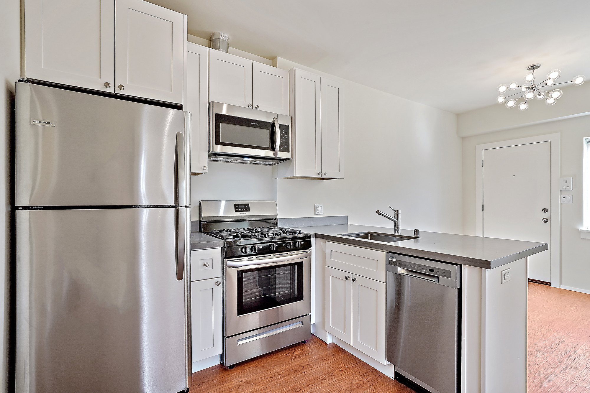 Kitchen with white cabinets, stainless steel refrigerator, microwave, oven, dishwasher, kitchen sink, and a modern ceiling chandelier.
