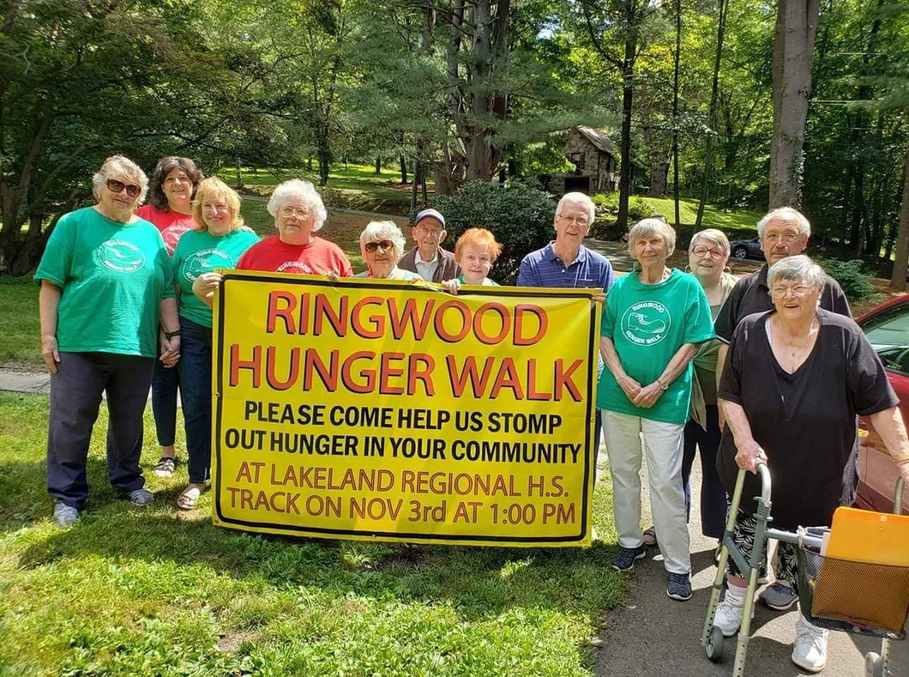 Group of seniors holding a yellow banner promoting the Ringwood Hunger Walk event in a park with trees.