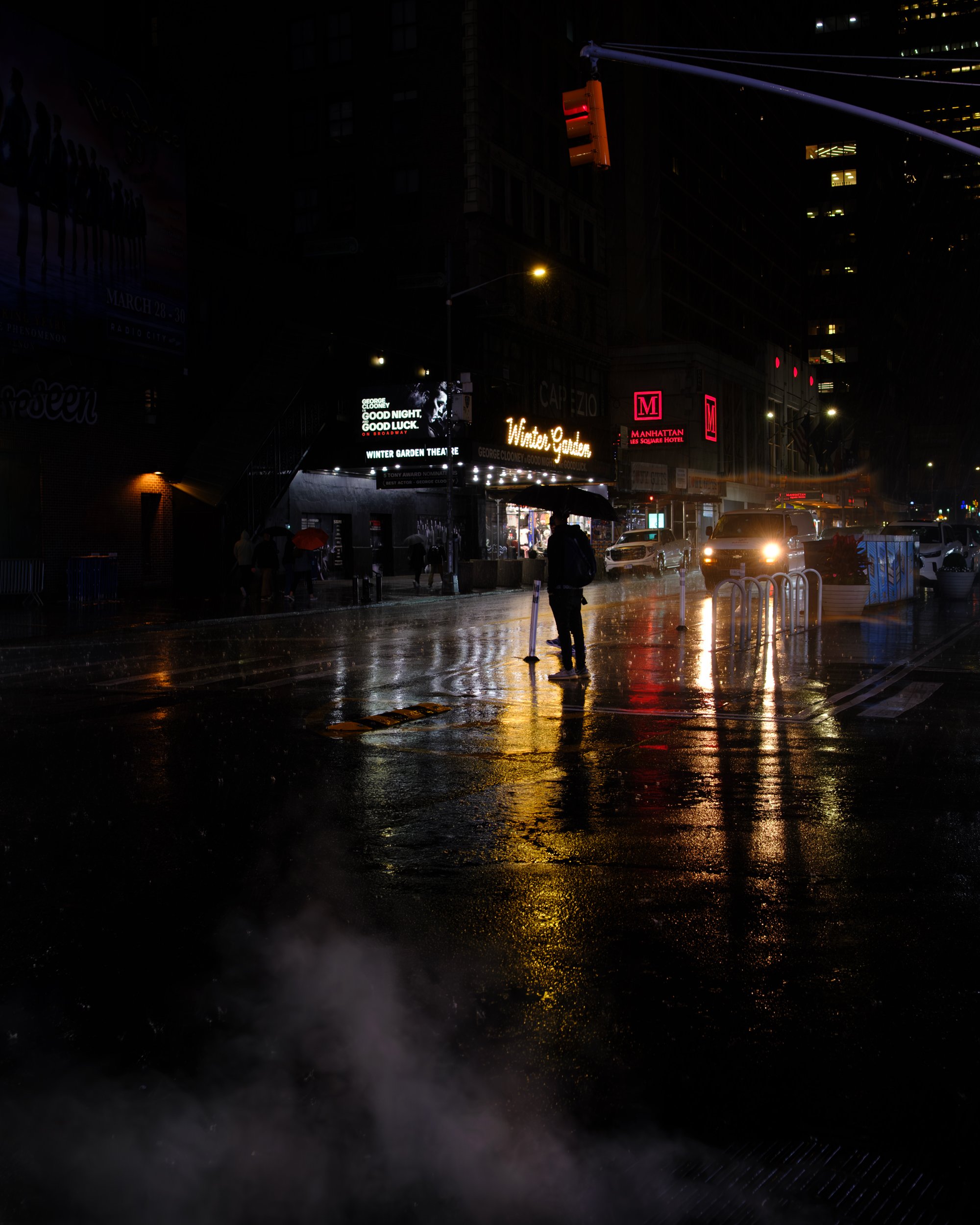 Night street scene with wet pavement reflecting colorful neon and traffic lights, presence of pedestrians with umbrellas, and illuminated signs on buildings.