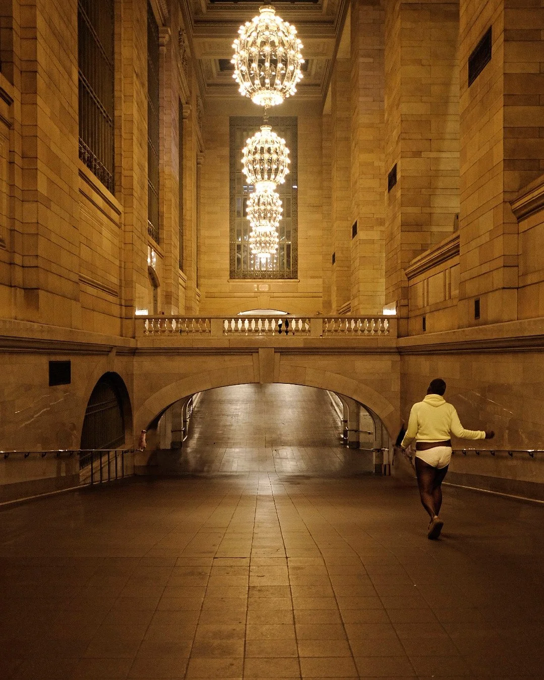 A person walking through a grand, illuminated hall with tall columns, chandeliers hanging from the ceiling, and an arched passageway.