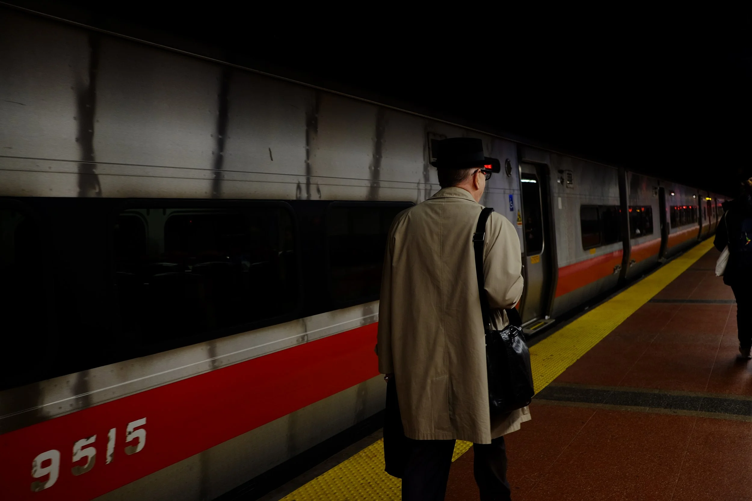 A person with a backpack and glasses stands on a train platform, waiting to board the train.