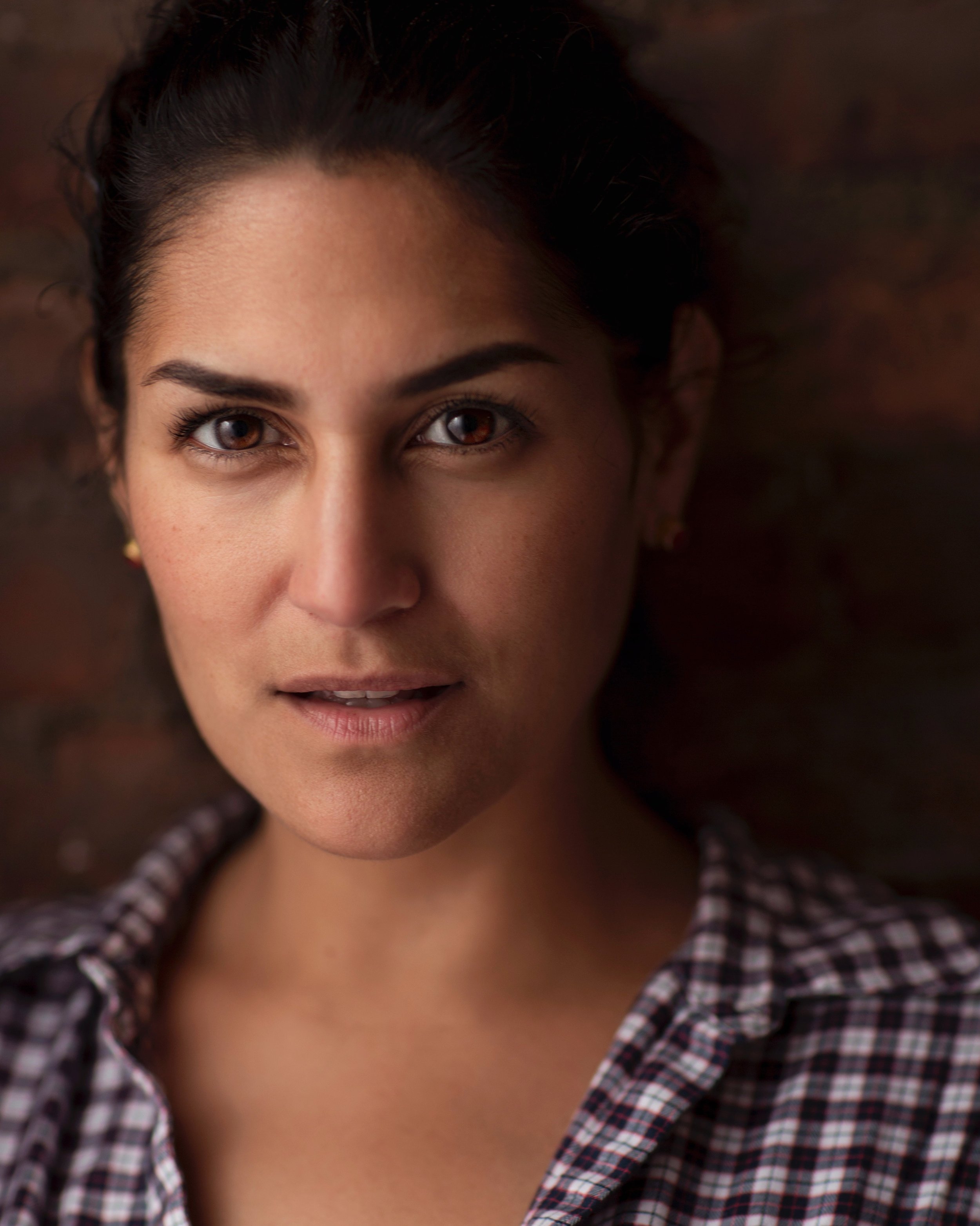 Close-up of a woman with brown hair, brown eyes, wearing a checkered shirt, lying on a wooden surface.