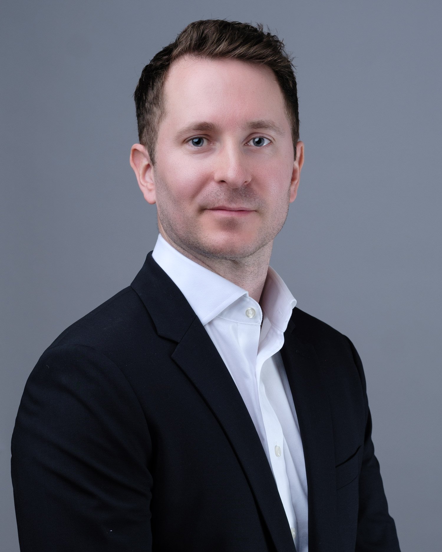 Portrait of a man in a black suit and white shirt against a gray background.