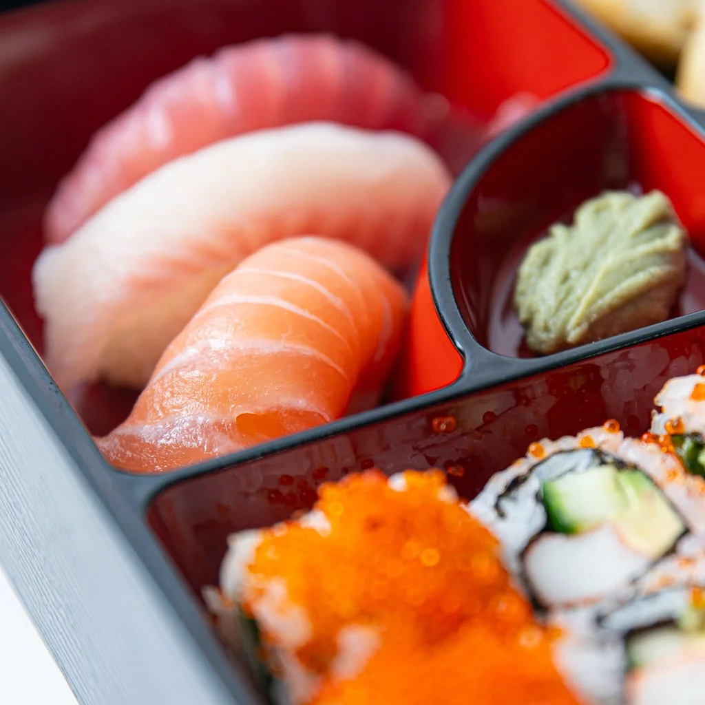 A bento box with slices of raw fish, wasabi, and sushi rolls with cucumber and fish roe. Sushi Photography Toronto