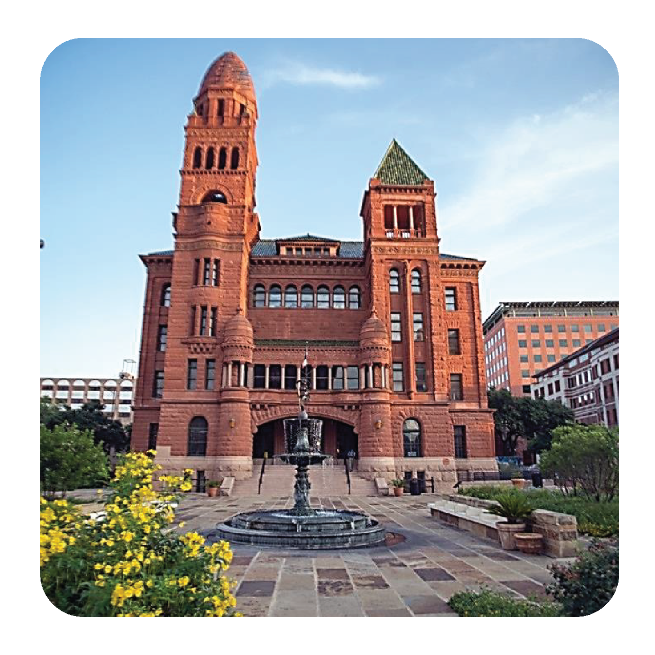 Red brick historic courthouse with two towers, a water fountain in front, and surrounding greenery.