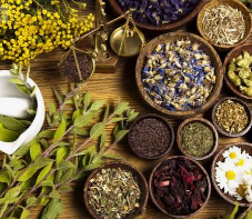 Disposición de varios ingredientes secos y flores aromáticas en pequeños recipientes de madera y cerámica sobre una mesa de madera.