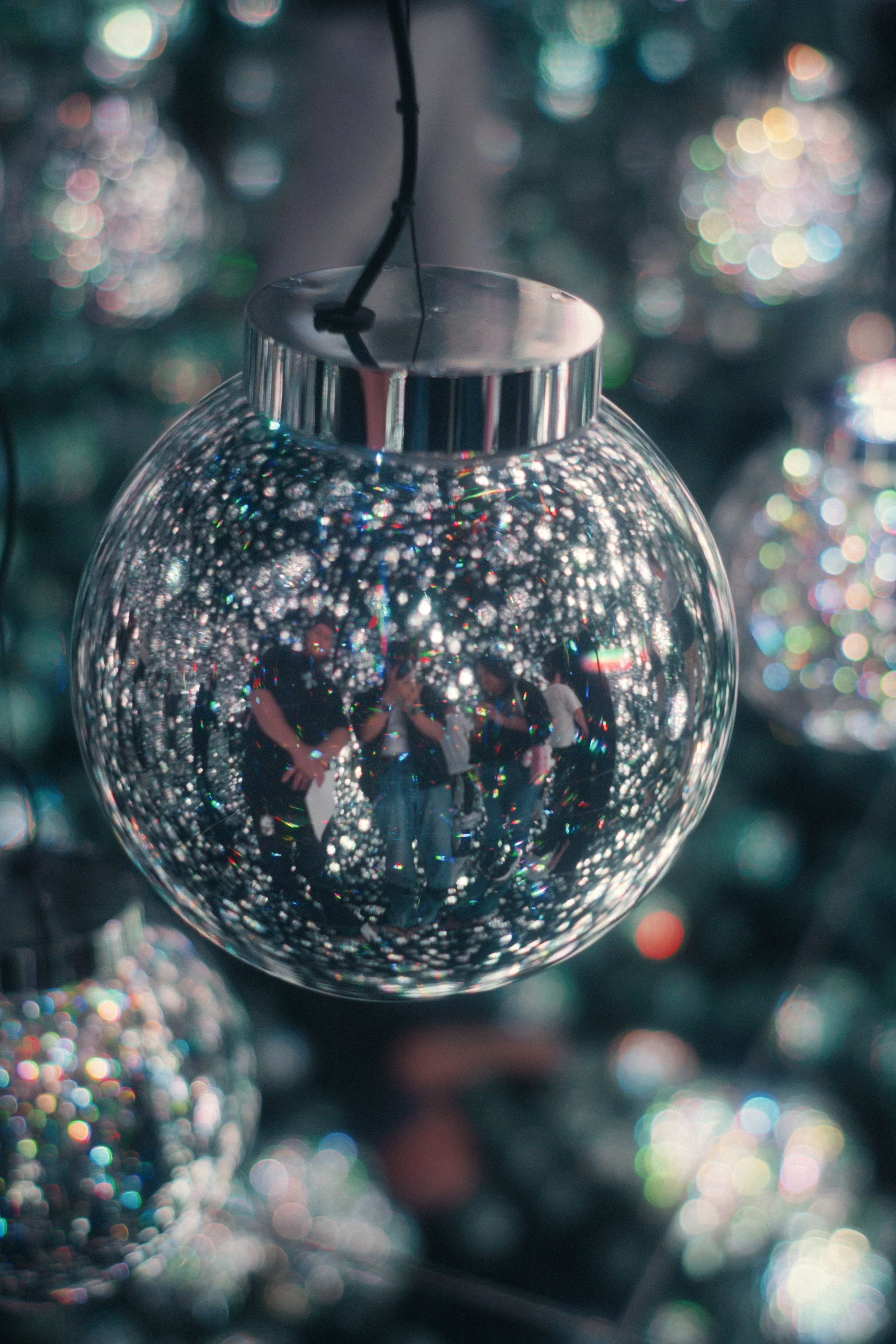 Close-up of a shiny silver Christmas ornament hanging on a tree with colorful lights in the blurred background.