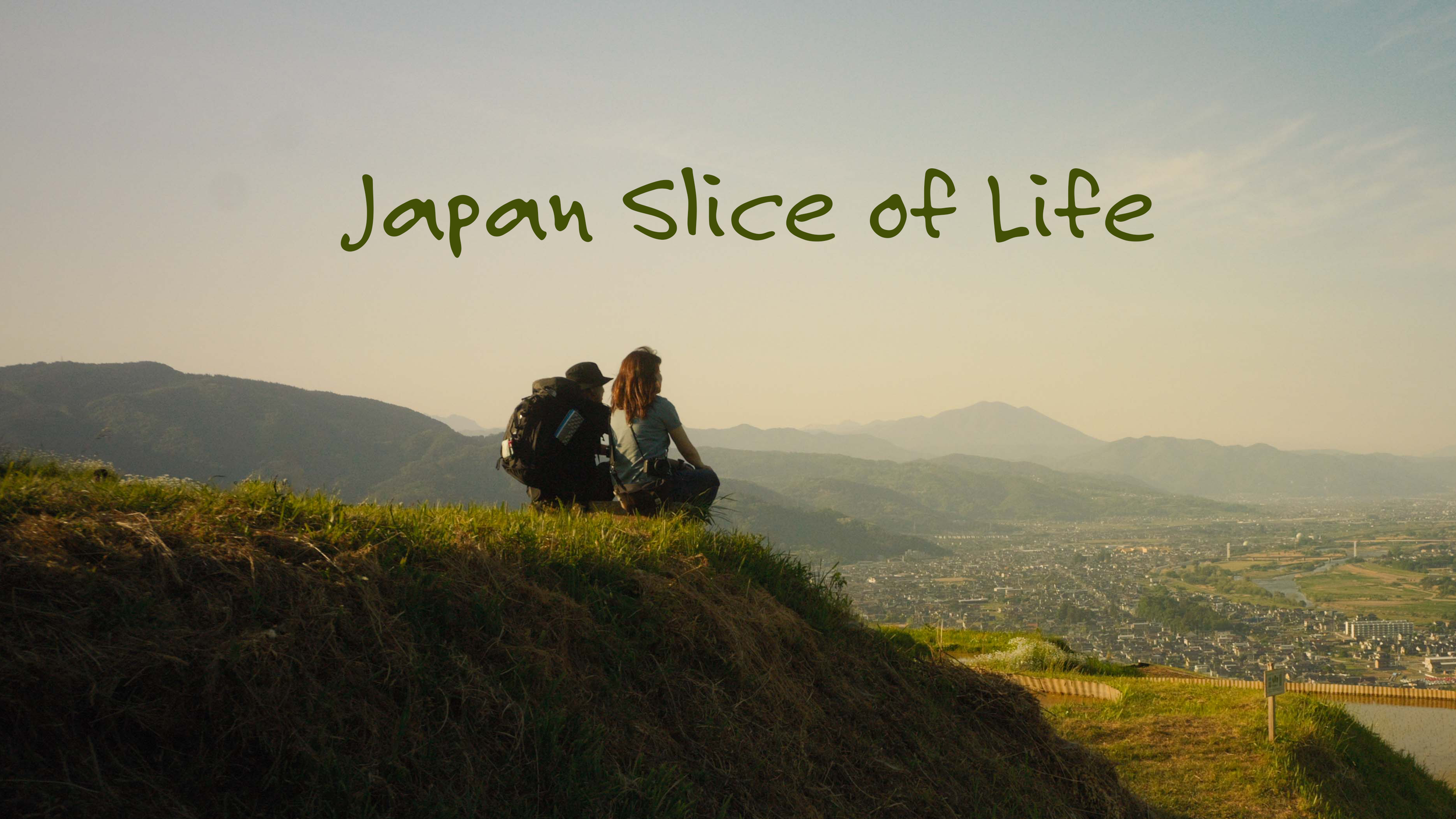 Two hikers sitting on a grassy hill overlooking a city and mountains, with the text 'Japan Slice of Life' over the sky.