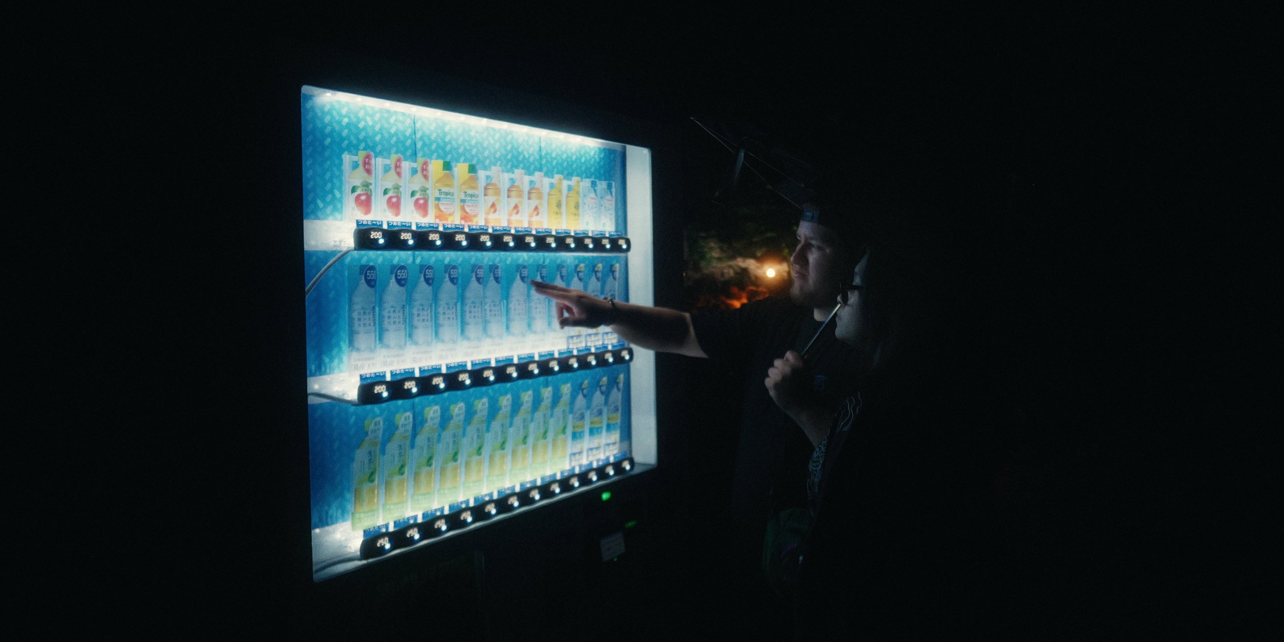 A person at night selecting a drink from a brightly lit vending machine.