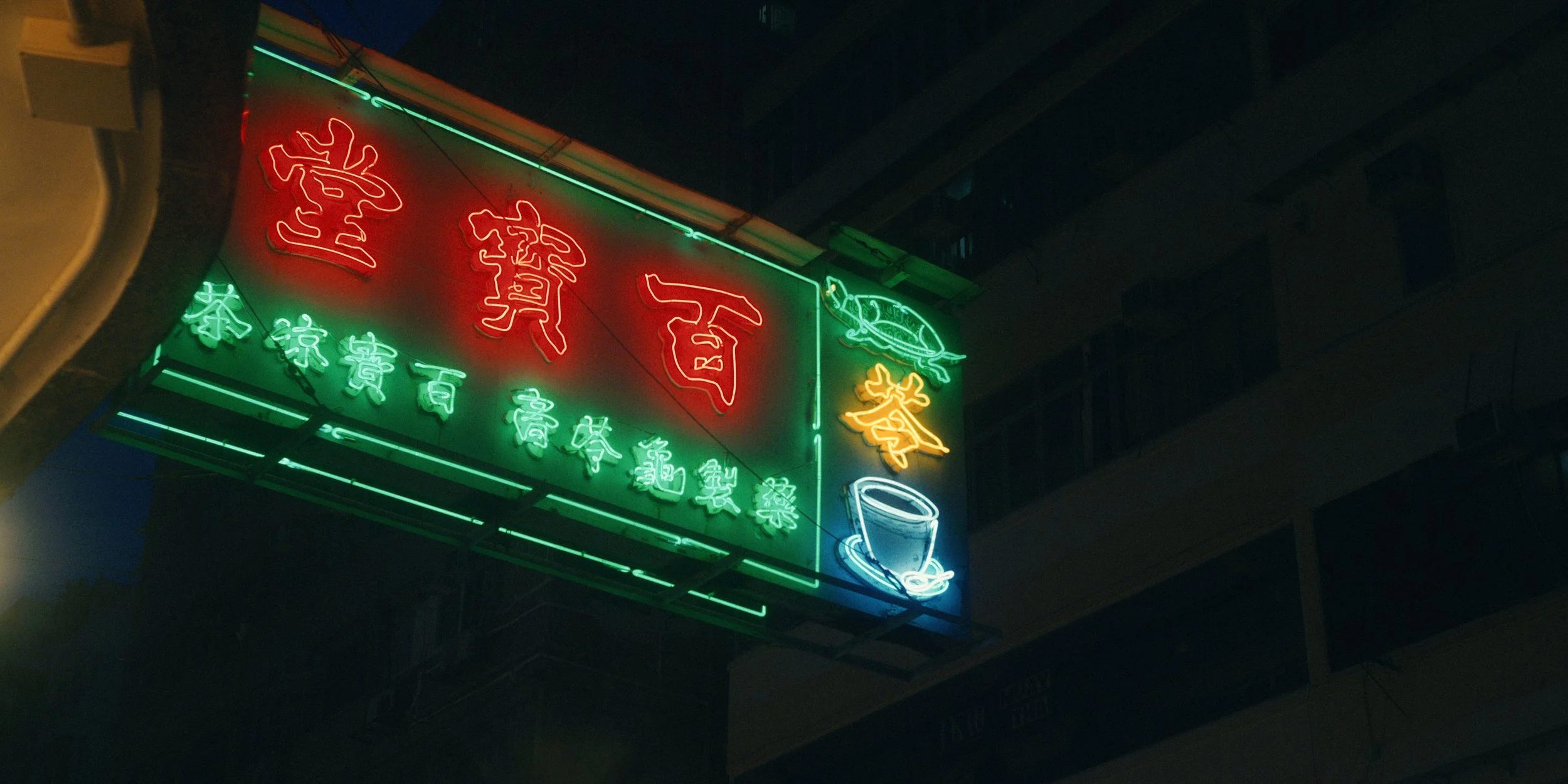 Neon signs with Chinese characters, a dragon, and a teacup symbol on a dark building exterior at night.