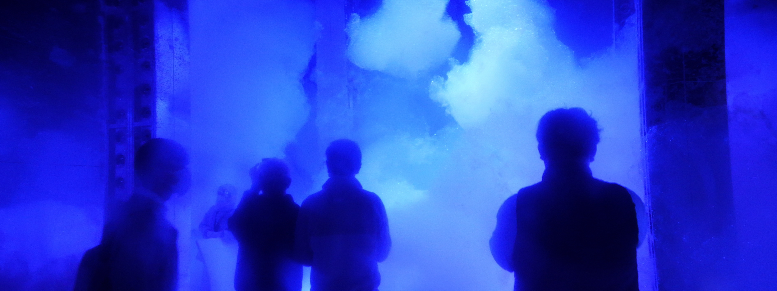 People standing inside an immersive blue-lit digital exhibit with fog and projections.