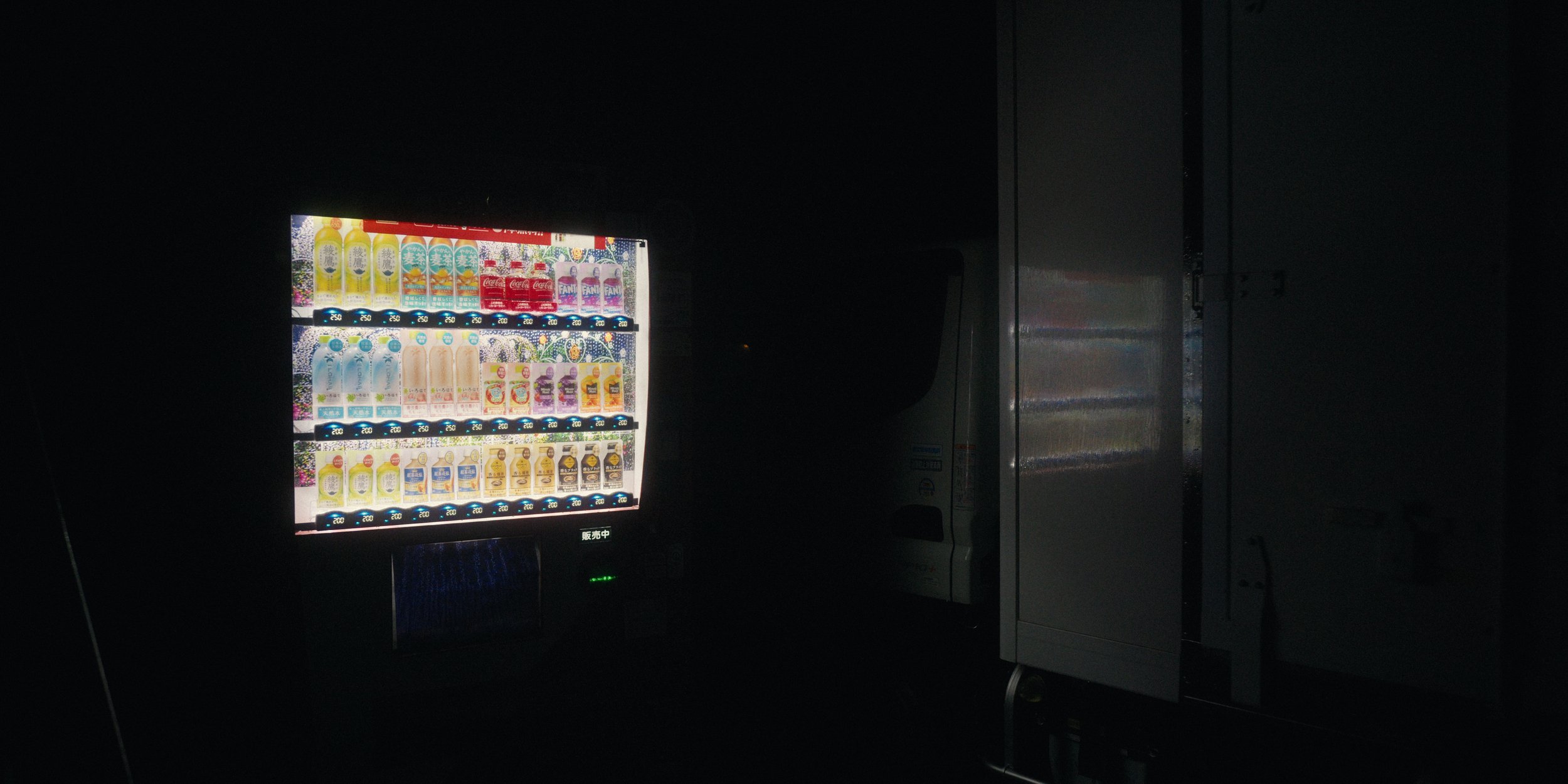 A vending machine stocked with various drinks, illuminated in a dark environment.
