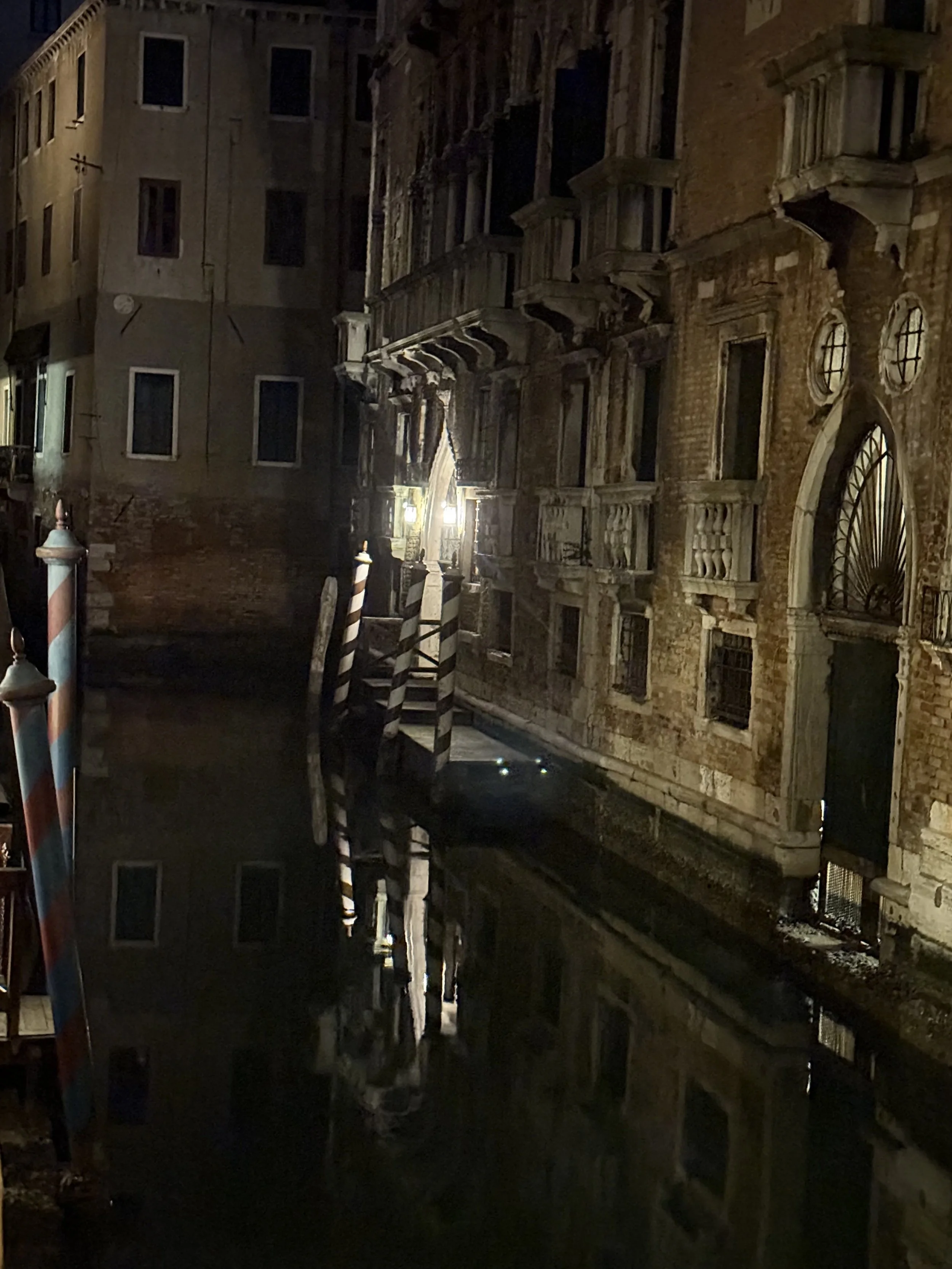Nighttime view of a canal with old buildings along the water, illuminated by streetlights, in Venice, Italy.